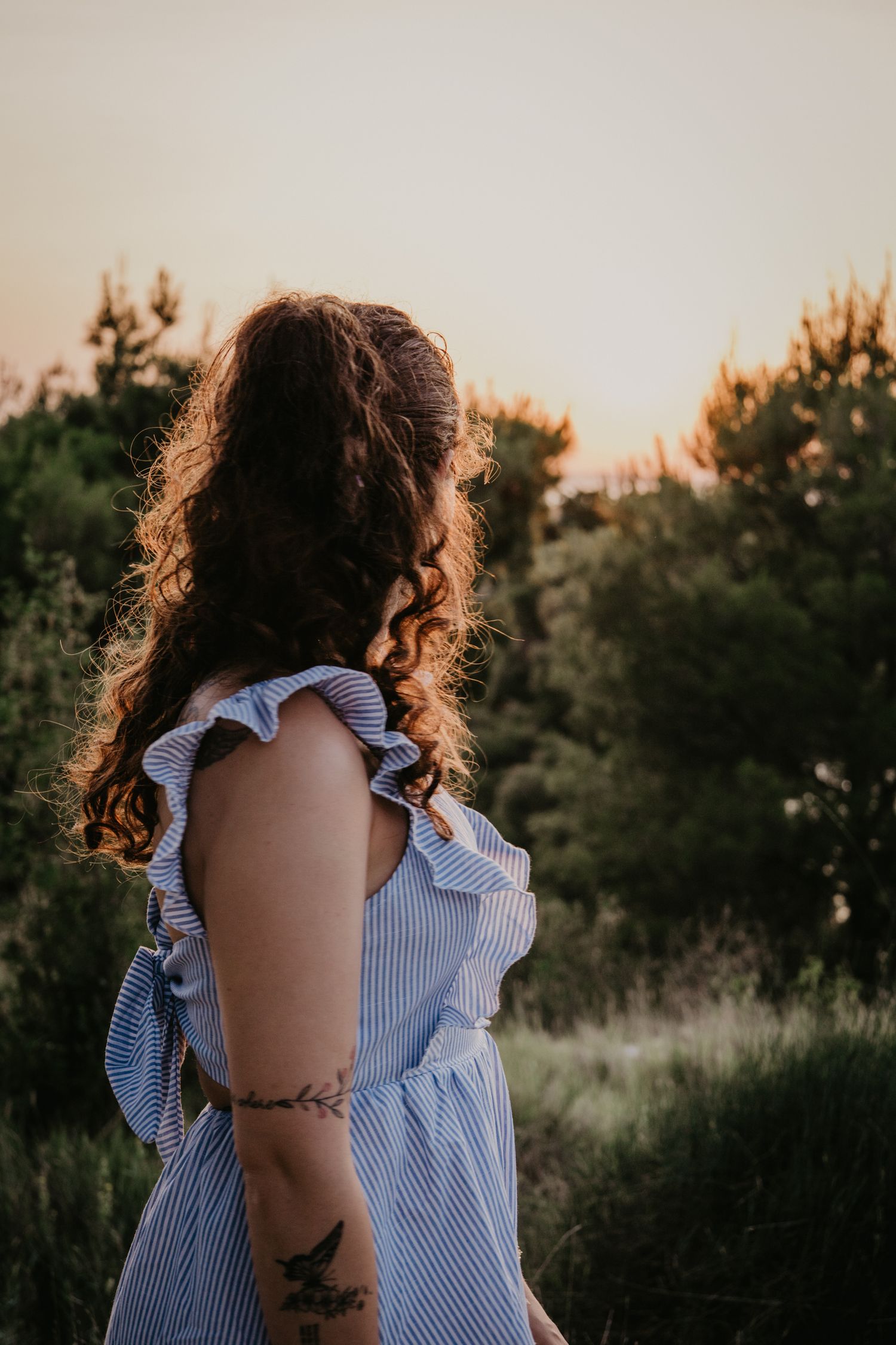Silhouette of person in ruffled blue striped shirt against sunset sky.