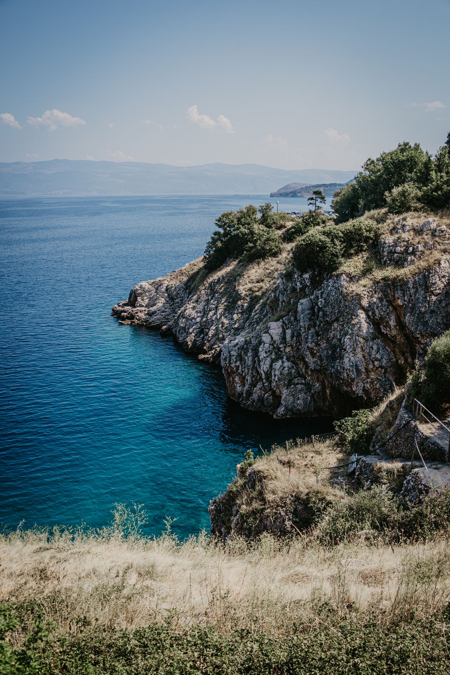 Dramatic coastal cliffs overlooking turquoise Mediterranean waters on a sunny day.