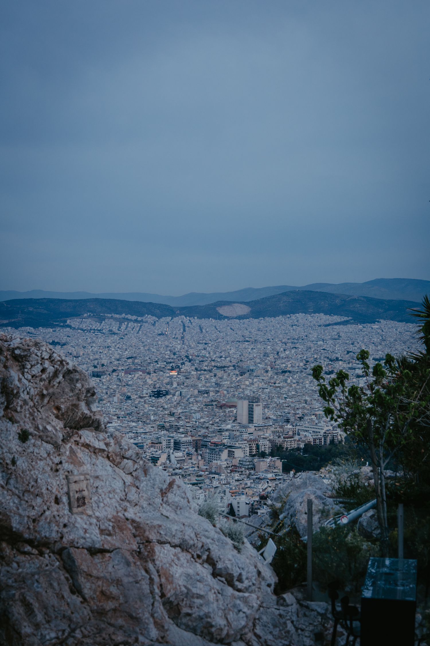 Panoramic cityscape view of Athens with mountains in the background under a blue sky.