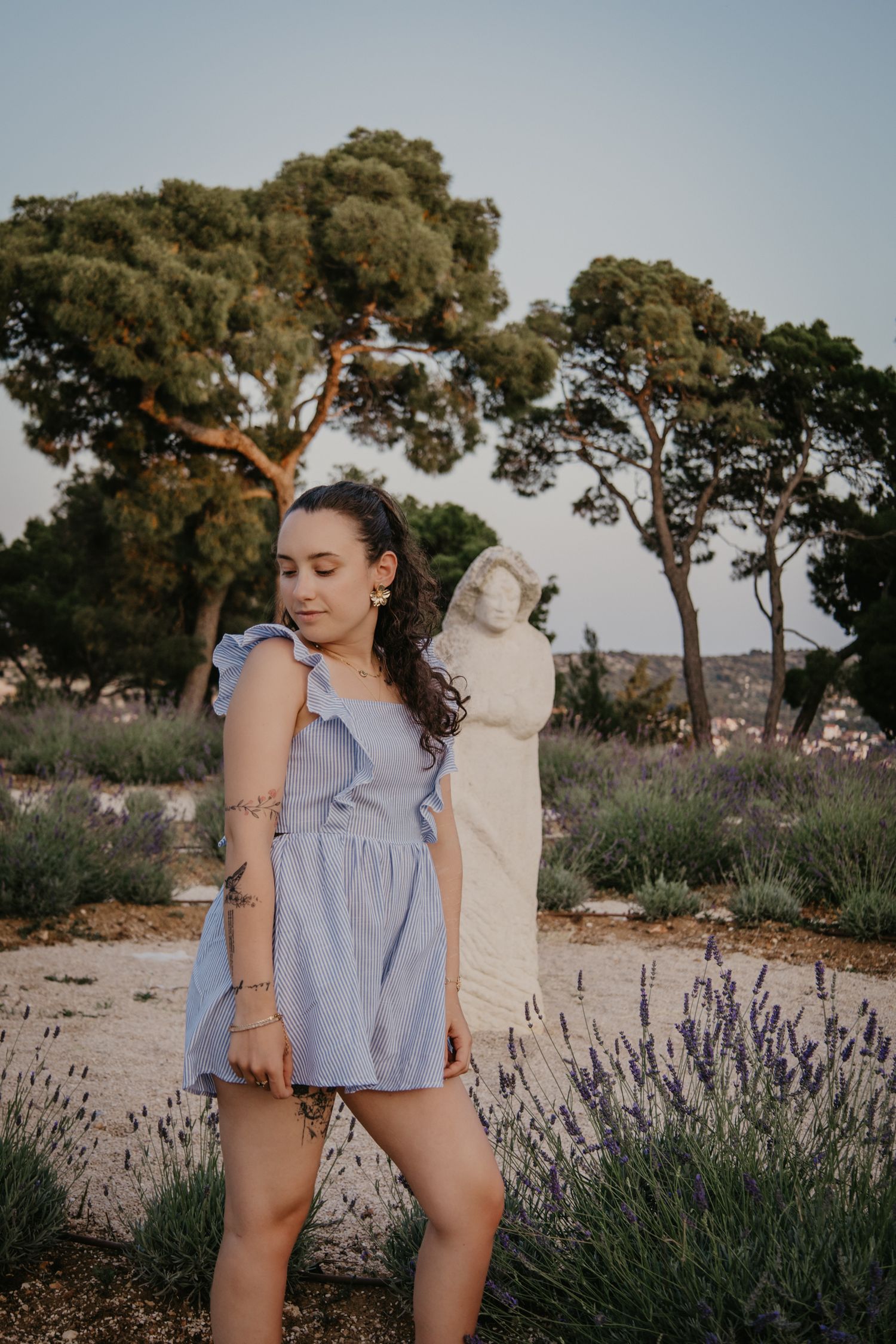 Person in blue striped outfit poses playfully in a lavender field at sunset.