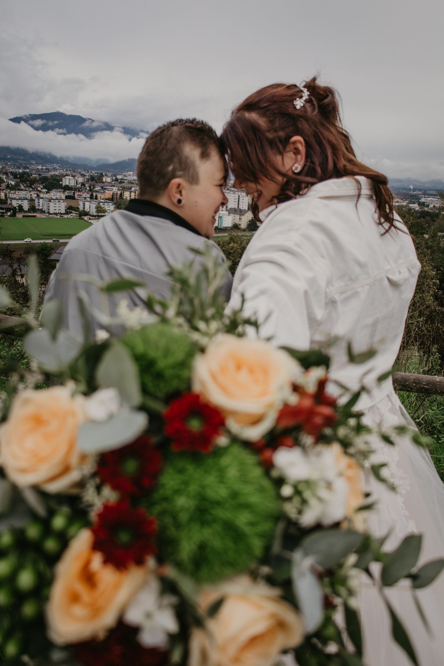 Wedding couple embracing with peach and burgundy floral bouquet in foreground.