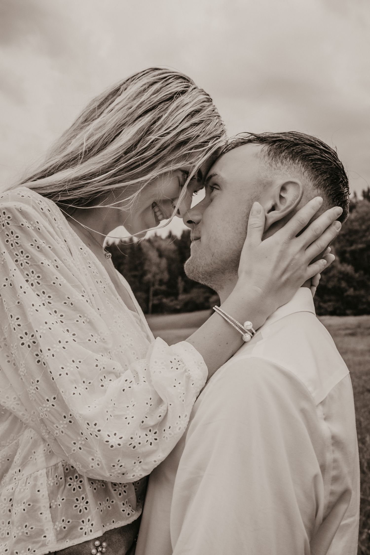 Black and white photo of a romantic couple sharing an intimate moment, woman in white lace dress cradling mans face.