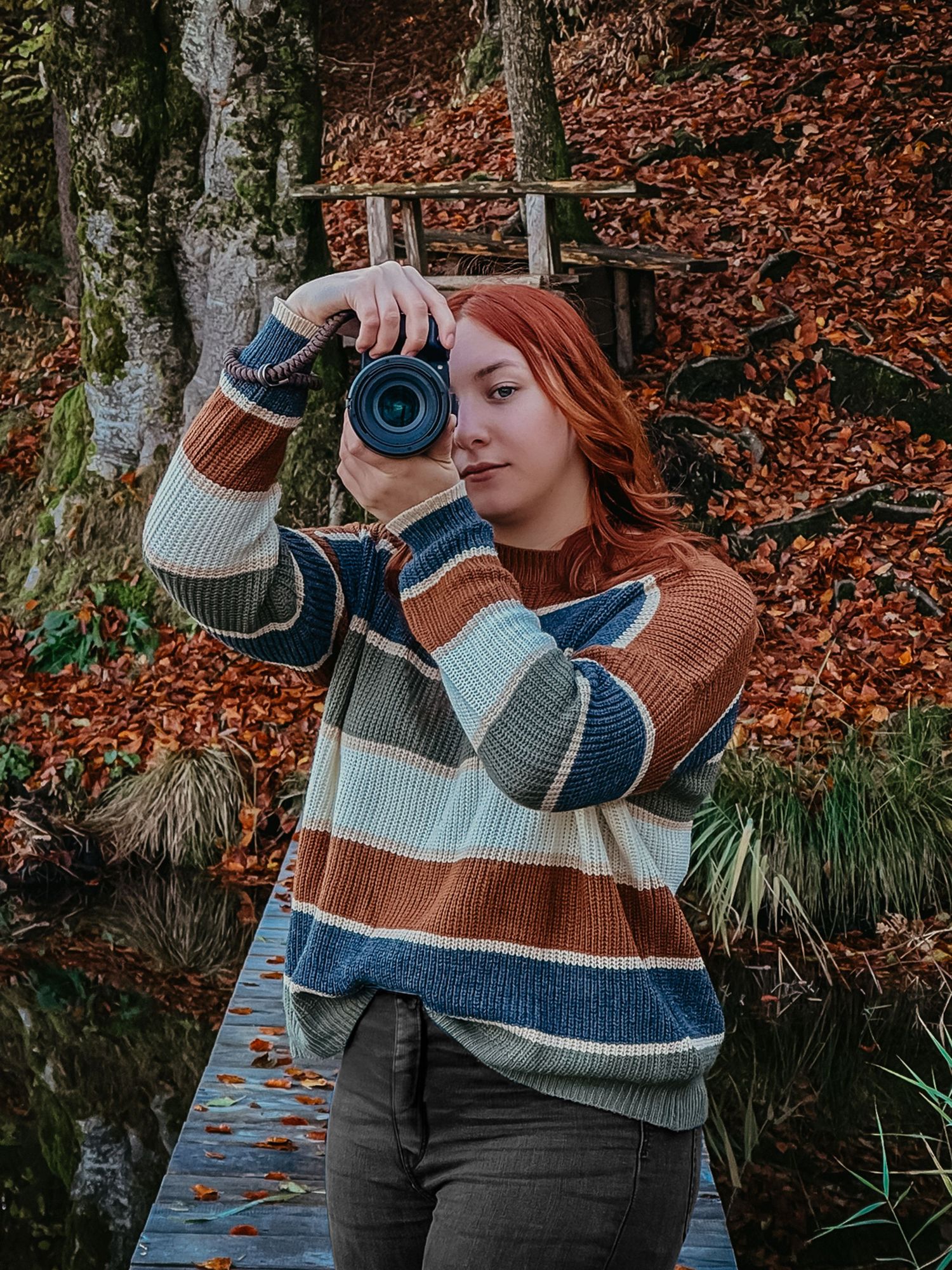 Fotografin in gestreiften Pullover mit Kamera in der Hand, vor herbstlichen Hintergrund.