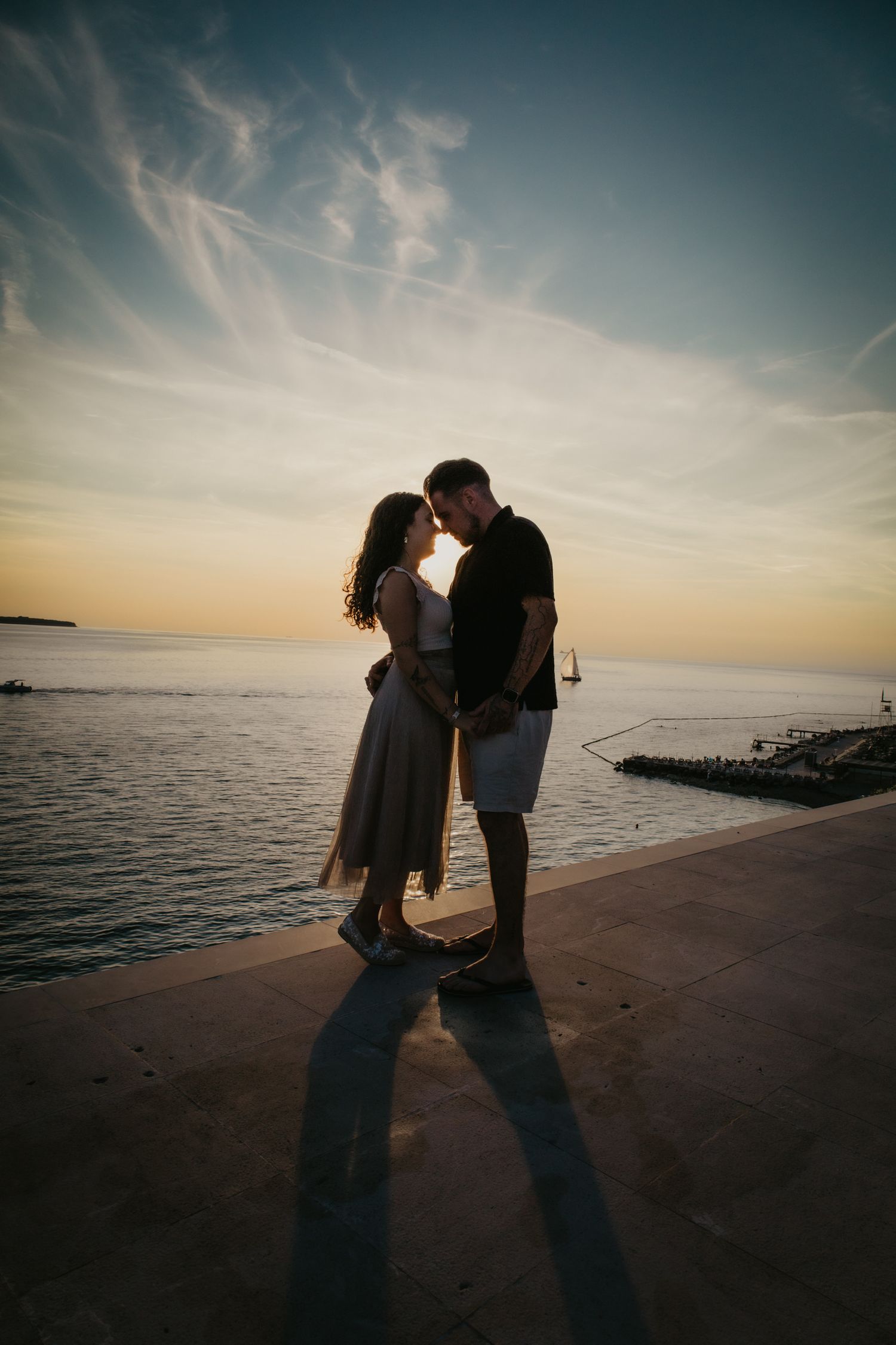 Silhouetted couple sharing romantic moments at sunset by the ocean.