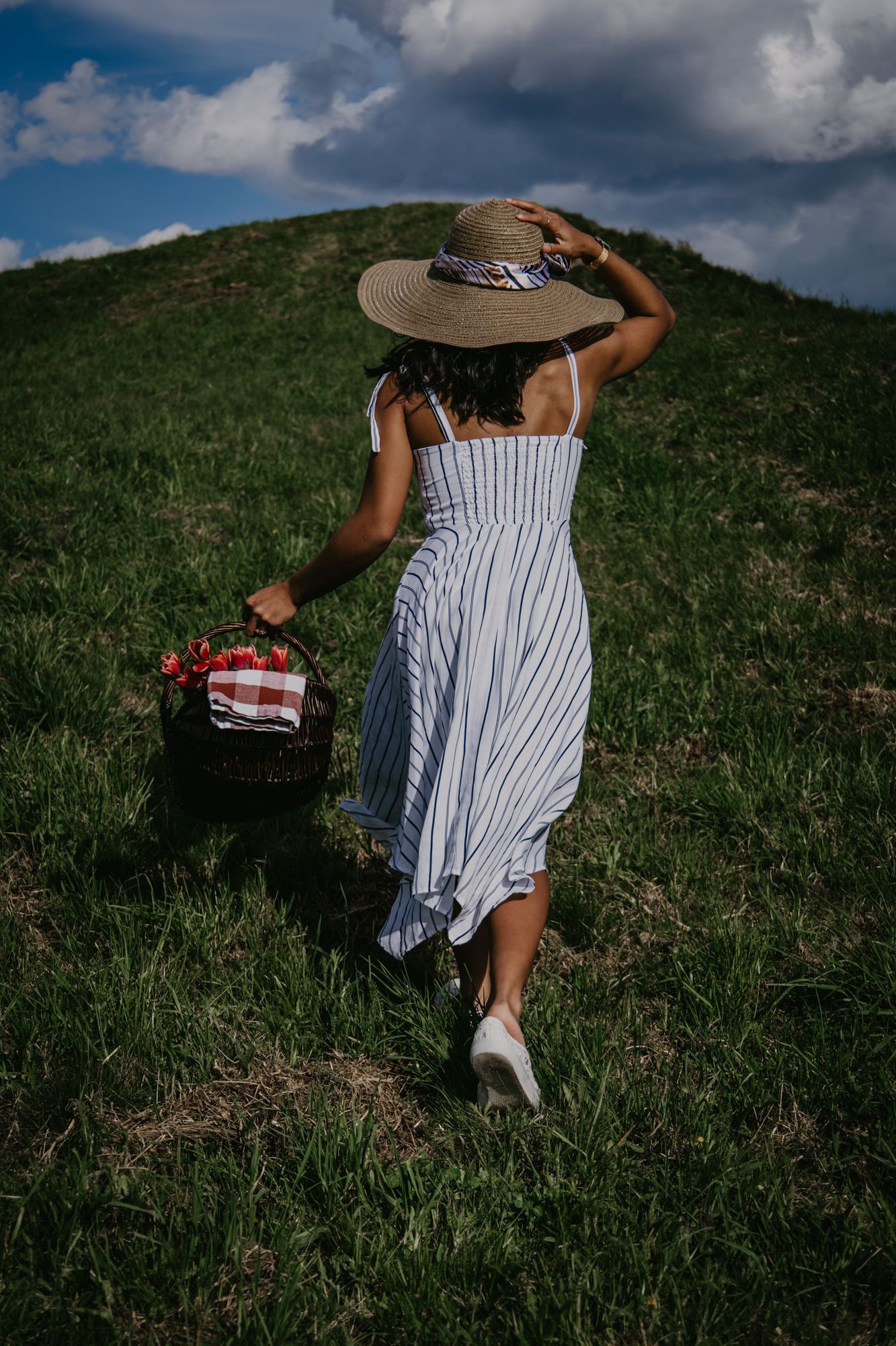 A person in a striped summer dress walking up a grassy hill on a sunny day.