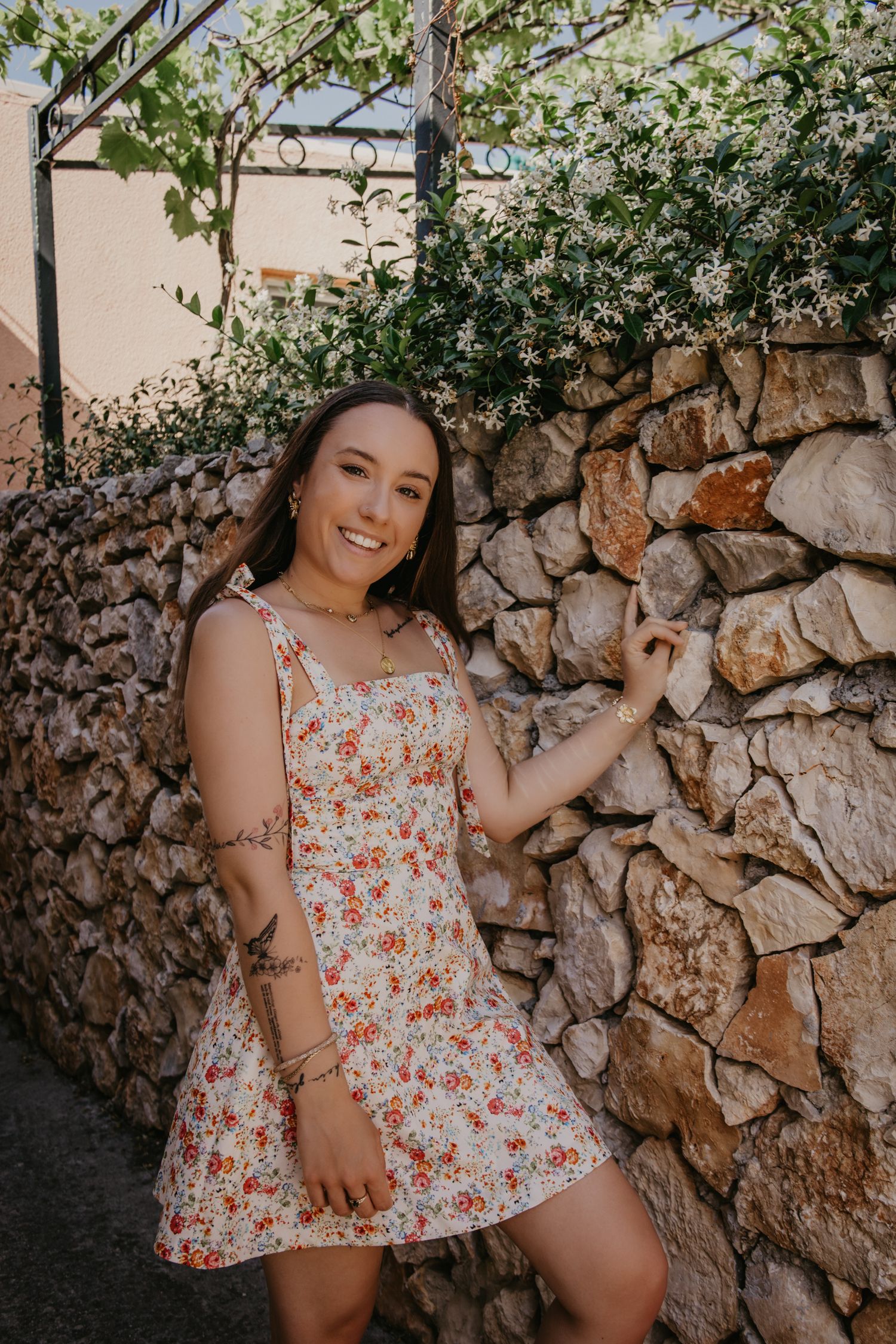Summer portrait against a rustic stone wall with green foliage overhead.