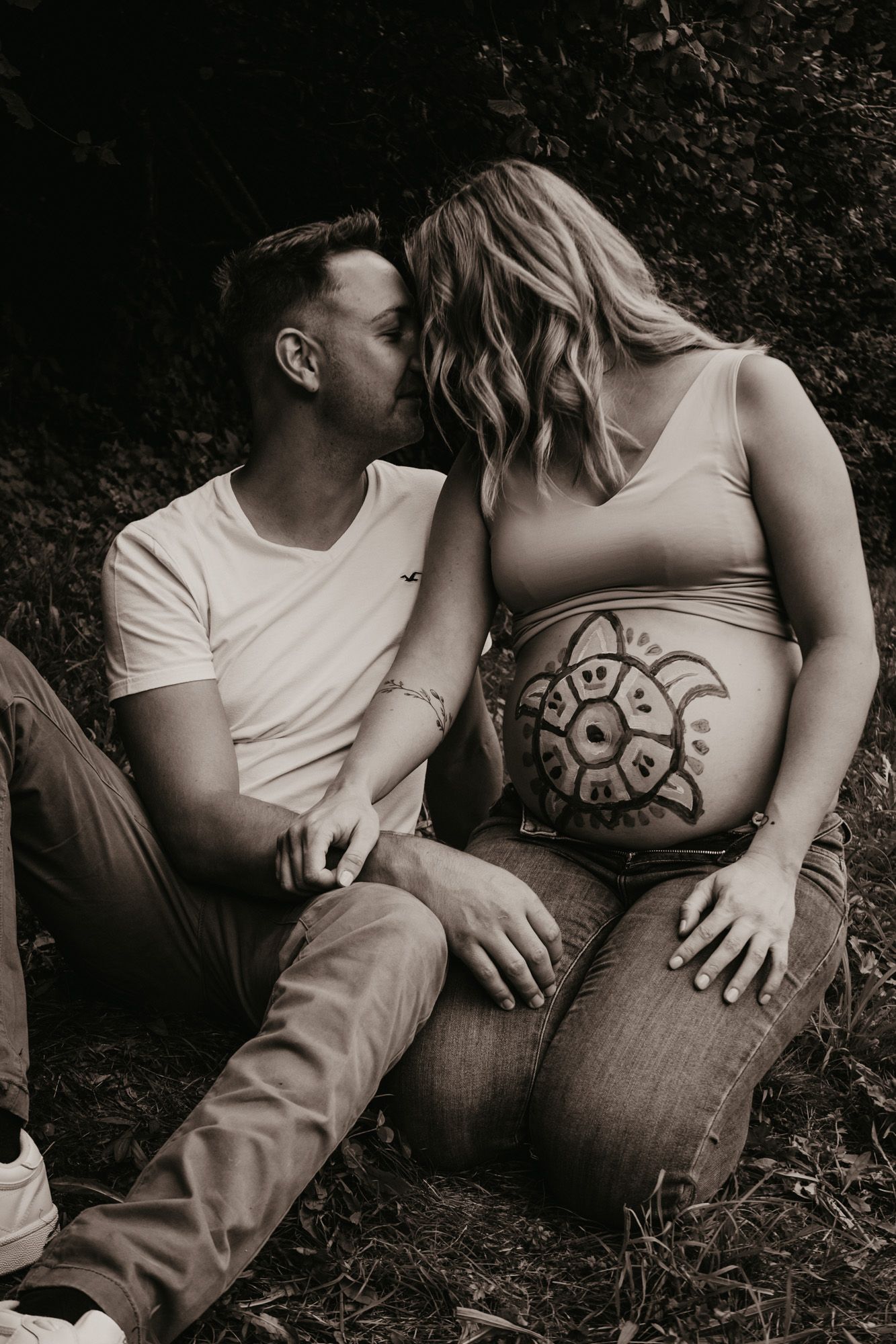 Black and white artistic maternity photos showing painted belly art in natural setting.