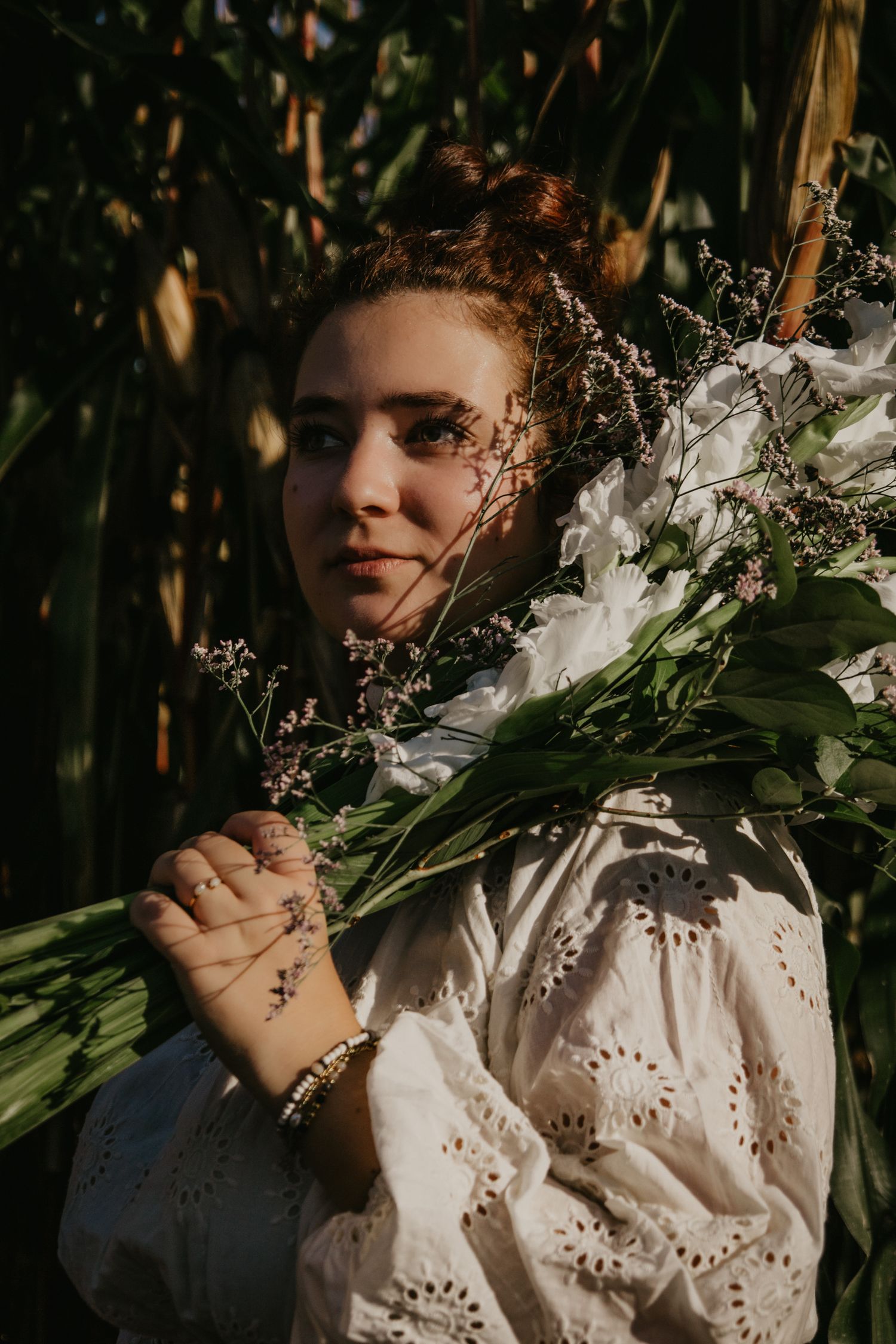 Close-up portrait with white flowers and lace dress details in a corn field setting.