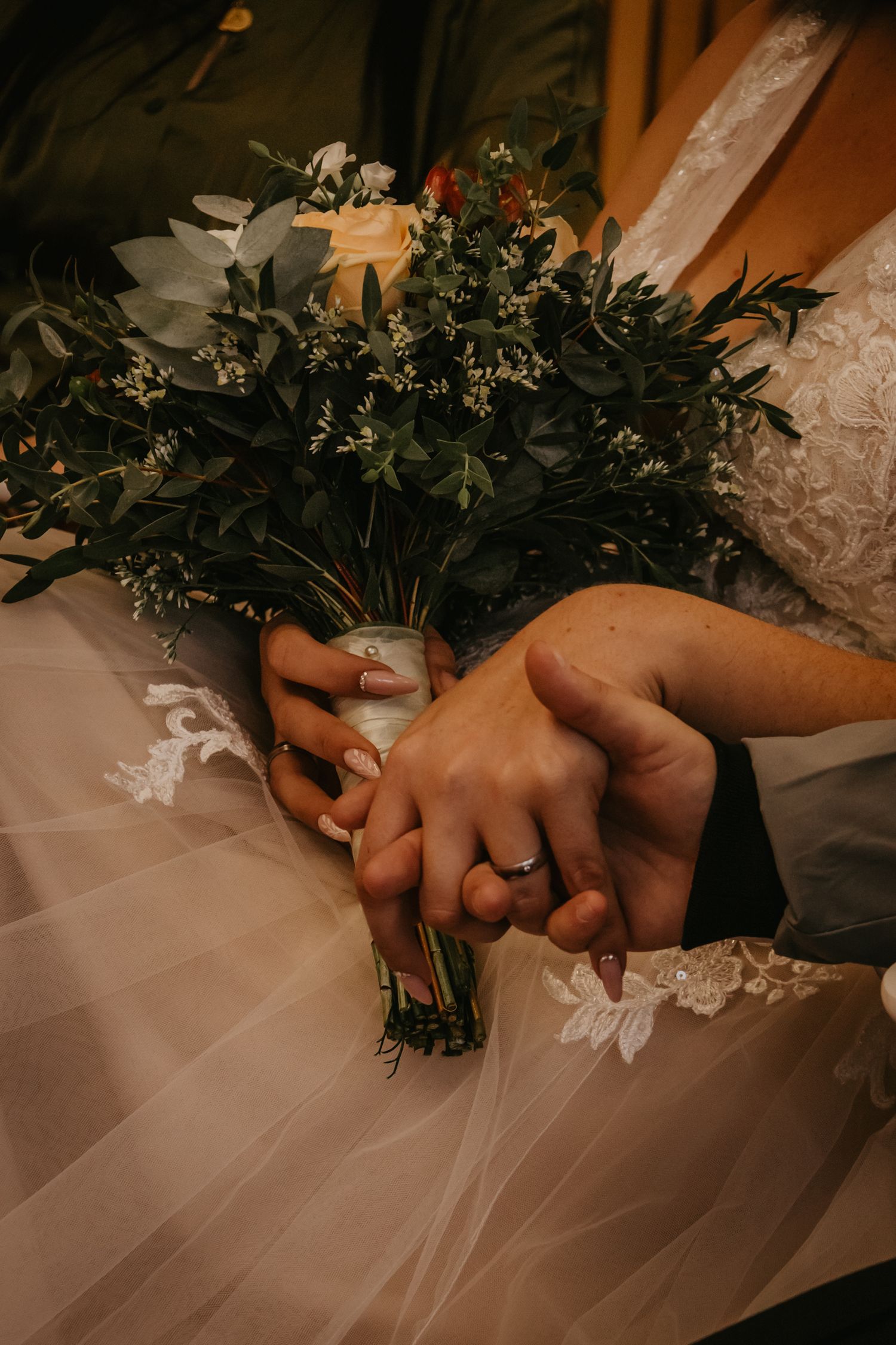 Close-up of newlyweds holding hands with wedding rings and bridal bouquet.