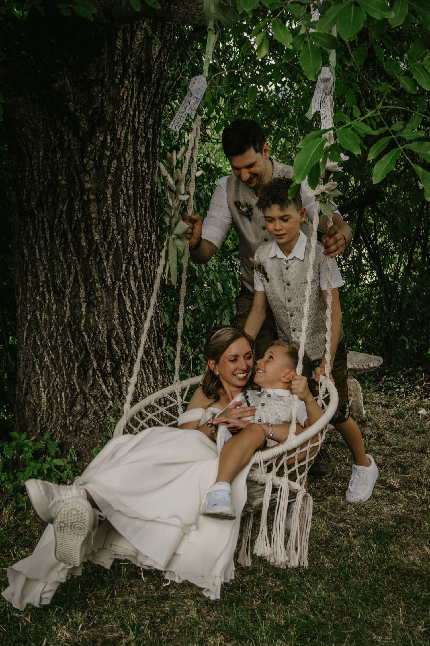 Wedding family portrait with bride holding baby on macrame swing surrounded by groom and son.