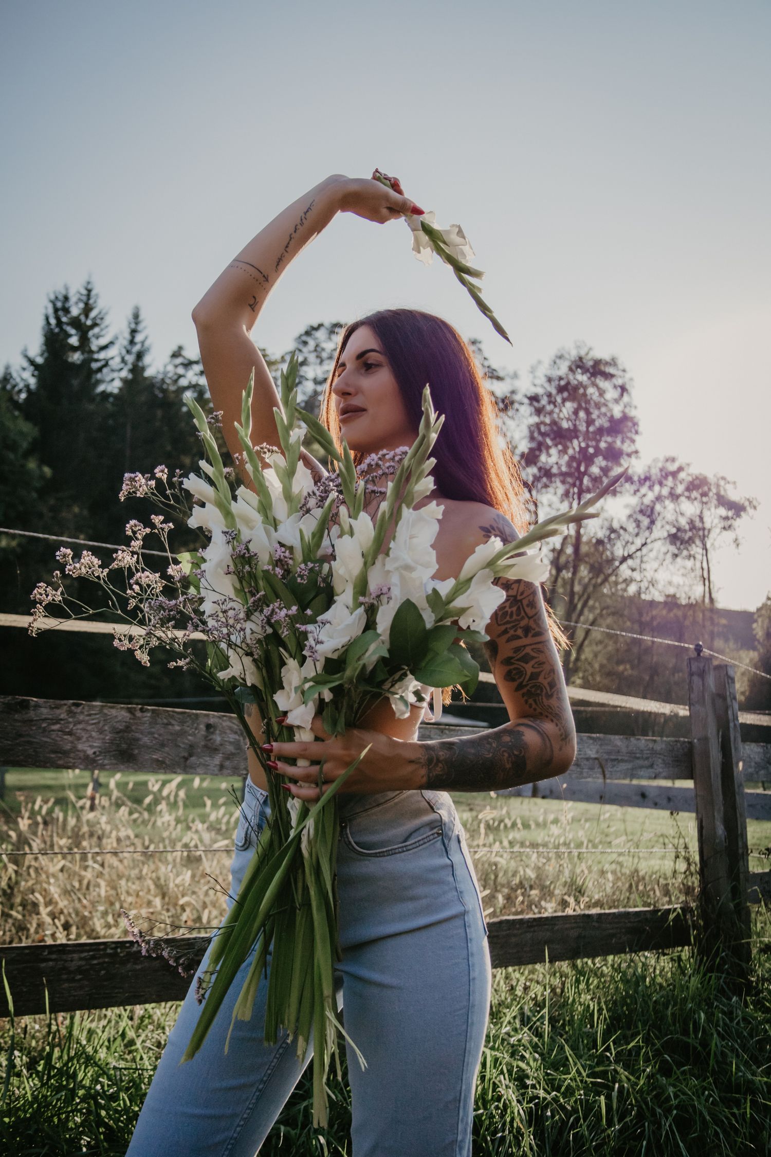 Artistic pose with bouquet of white gladiolus flowers in casual denim against wooden fence.