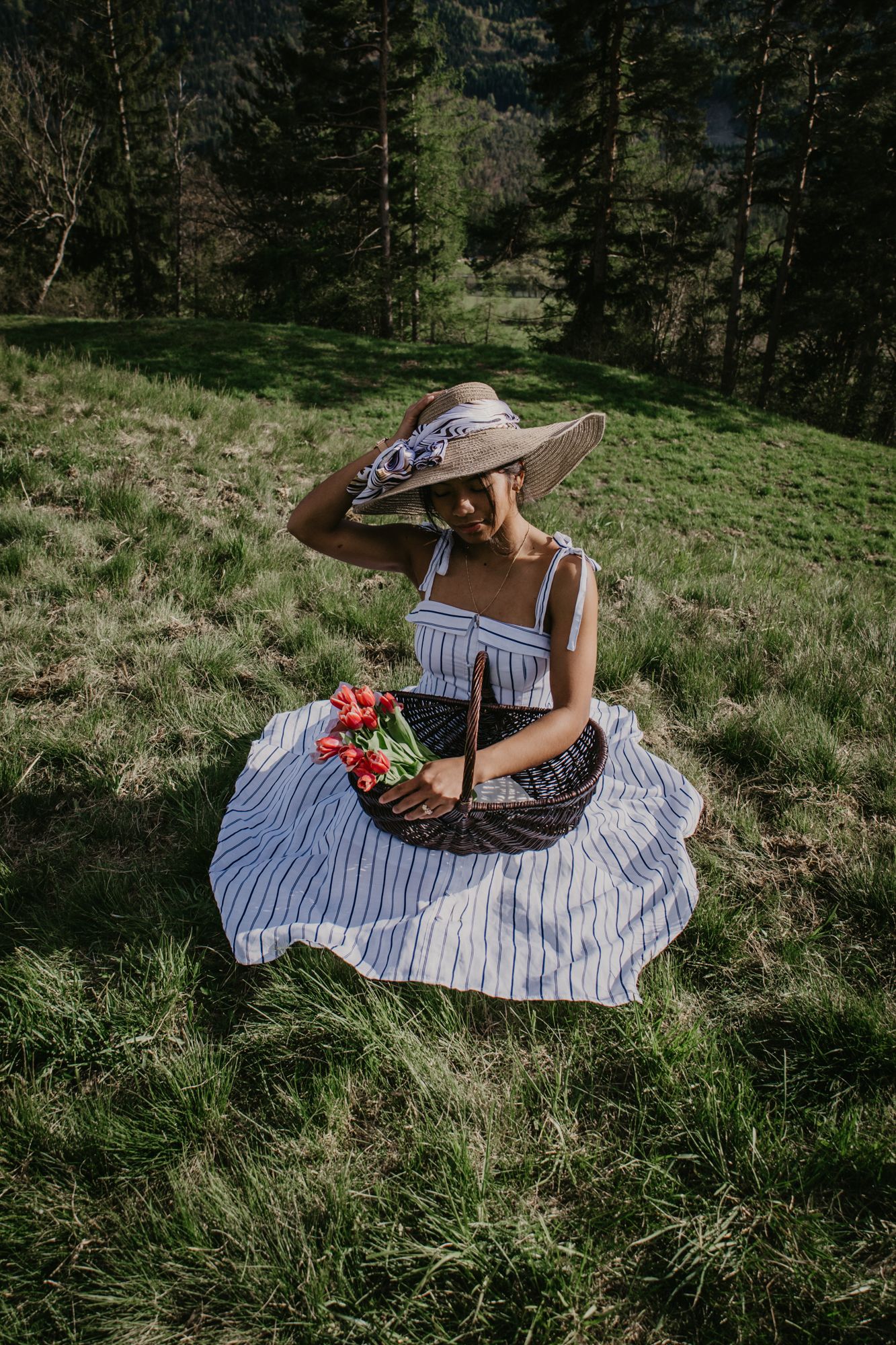 Lounging in grass wearing sunhat and striped dress on mountainside.