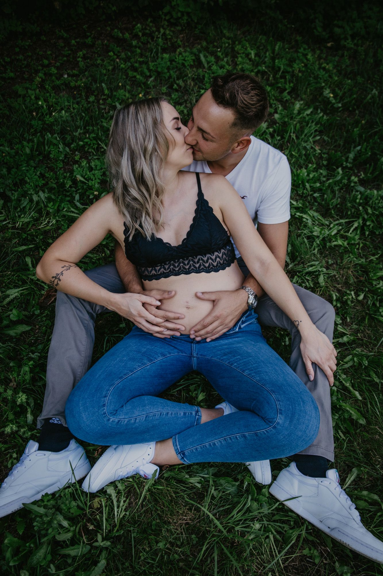 An intimate maternity photoshoot of a couple sitting on grass.