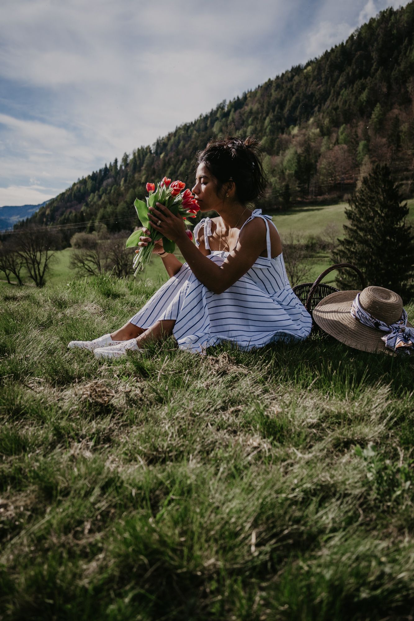 Person in white dress lying in mountain meadow grass with red flowers.