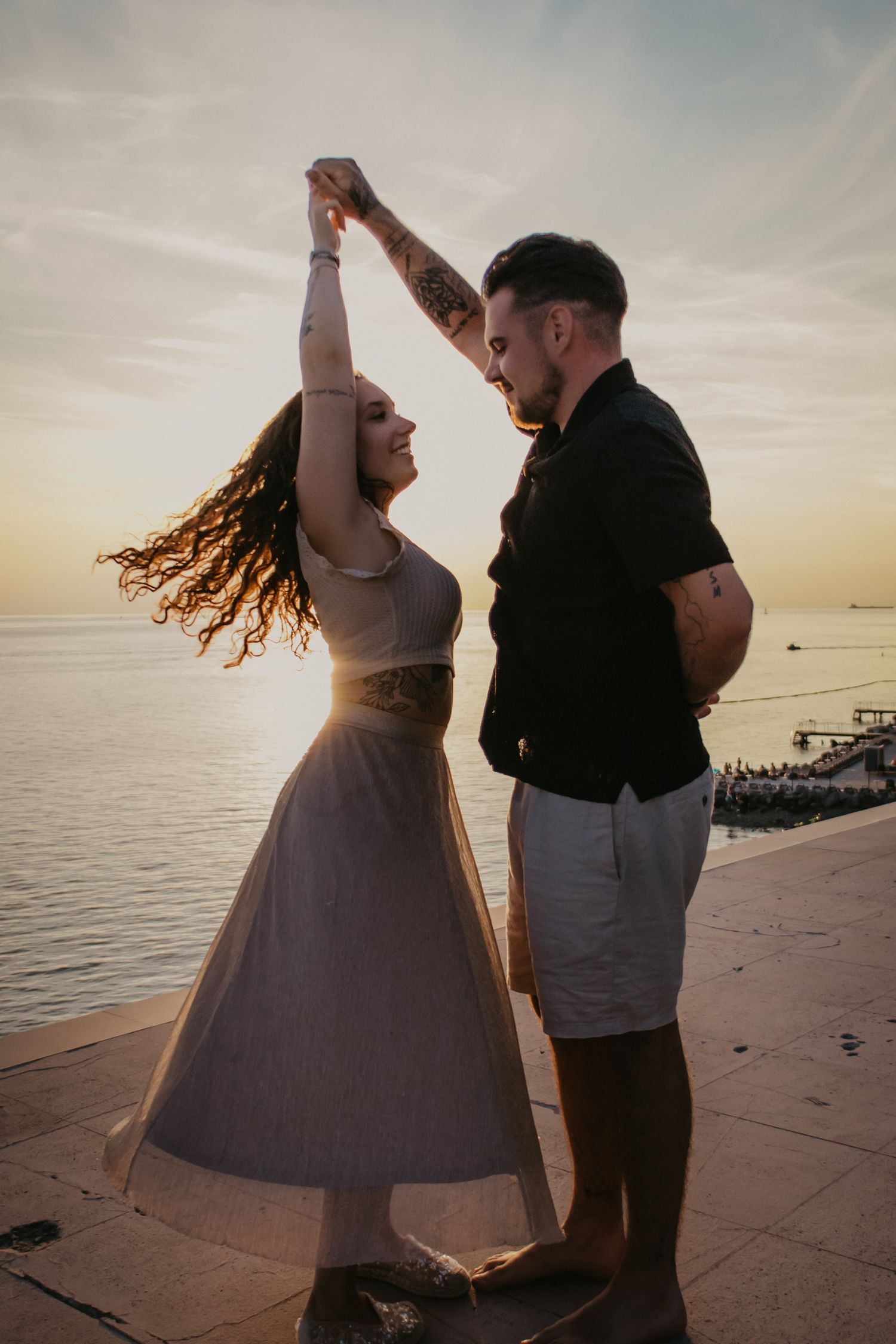 A couple dances playfully on a lakeside pier at sunset with flowing movement.