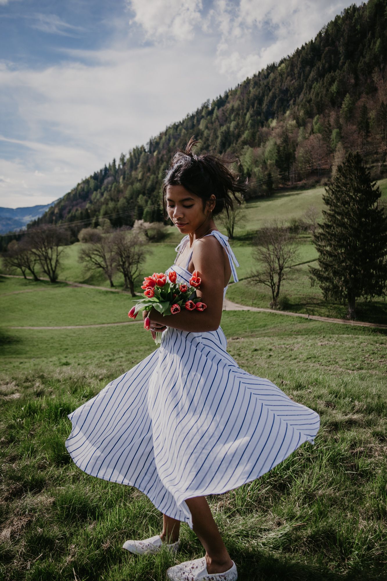 A white striped sundress twirls against a mountain landscape with vibrant red tulips.