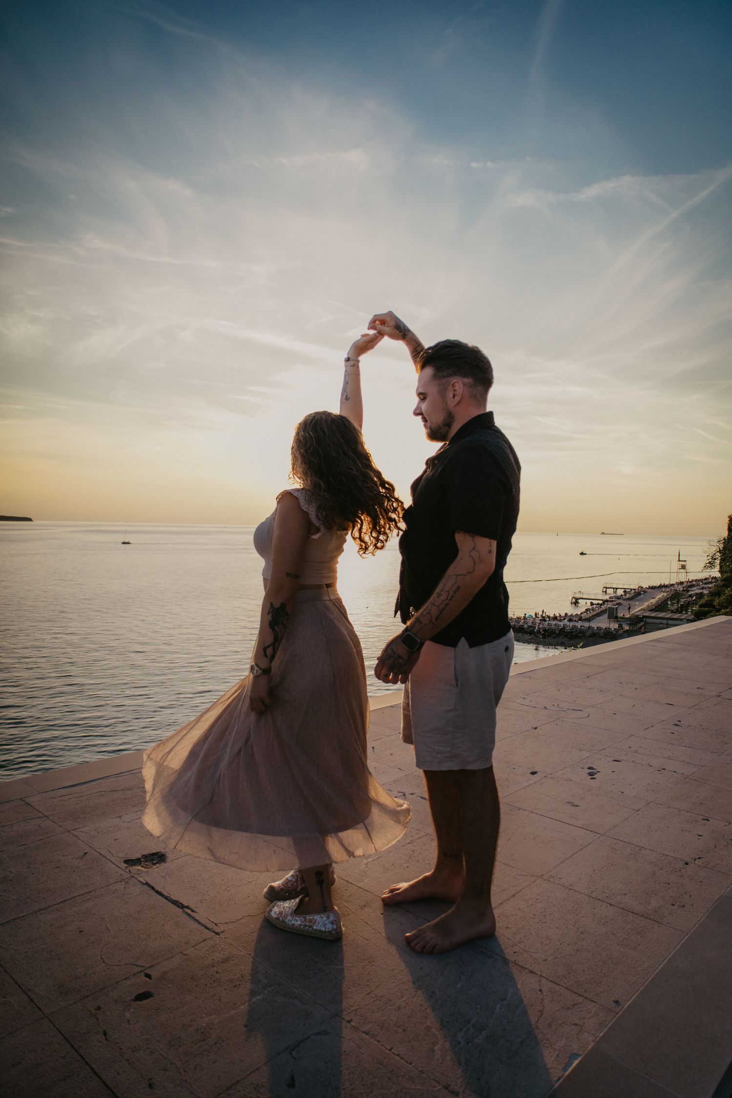 Two people dance together on a waterfront pier during golden hour.