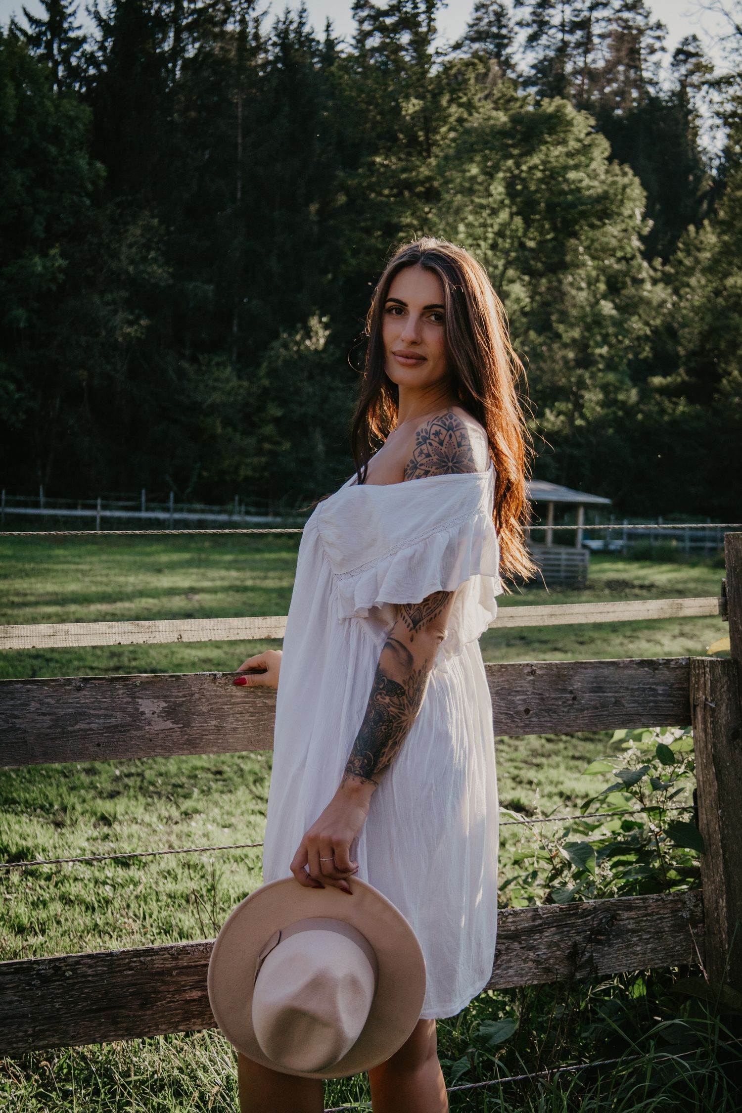 Artistic portrait in a white dress against a pastoral farm setting with evergreen trees.