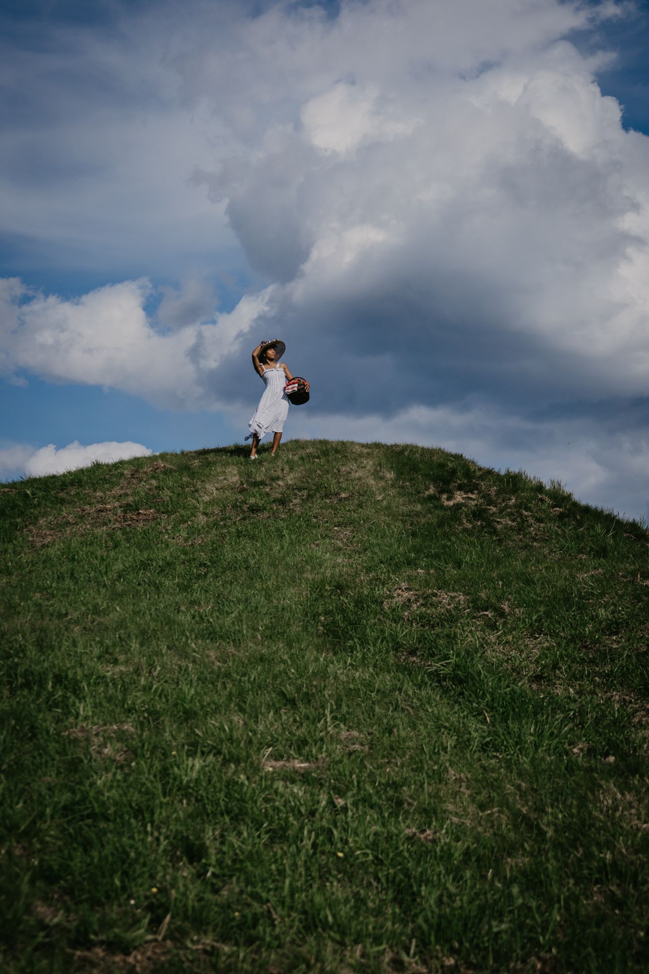 A grassy hillside with dramatic cloudy sky and mountain views in the background.