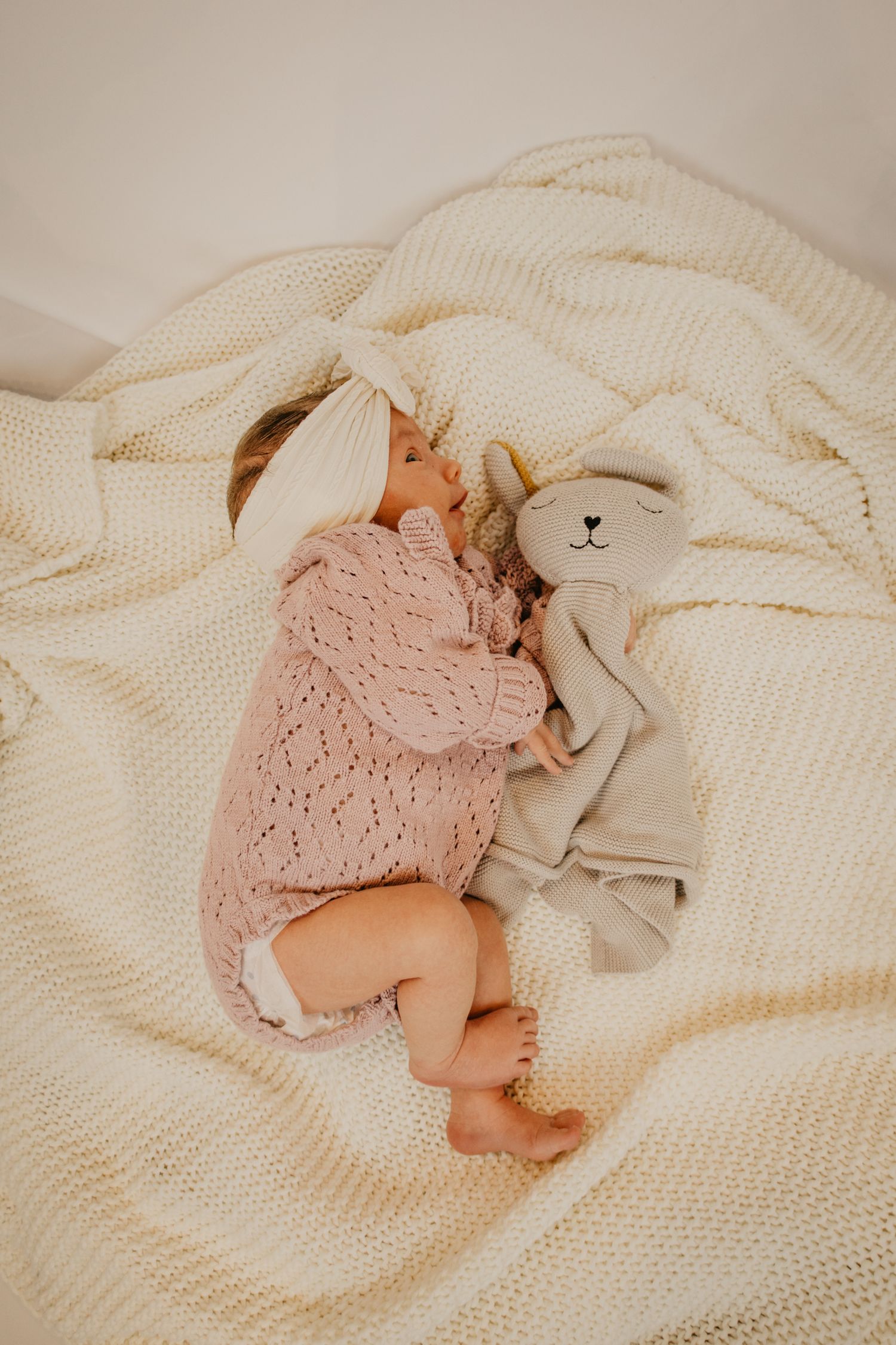 Baby sleeping peacefully on white knit blanket with plush bunny toy companion.