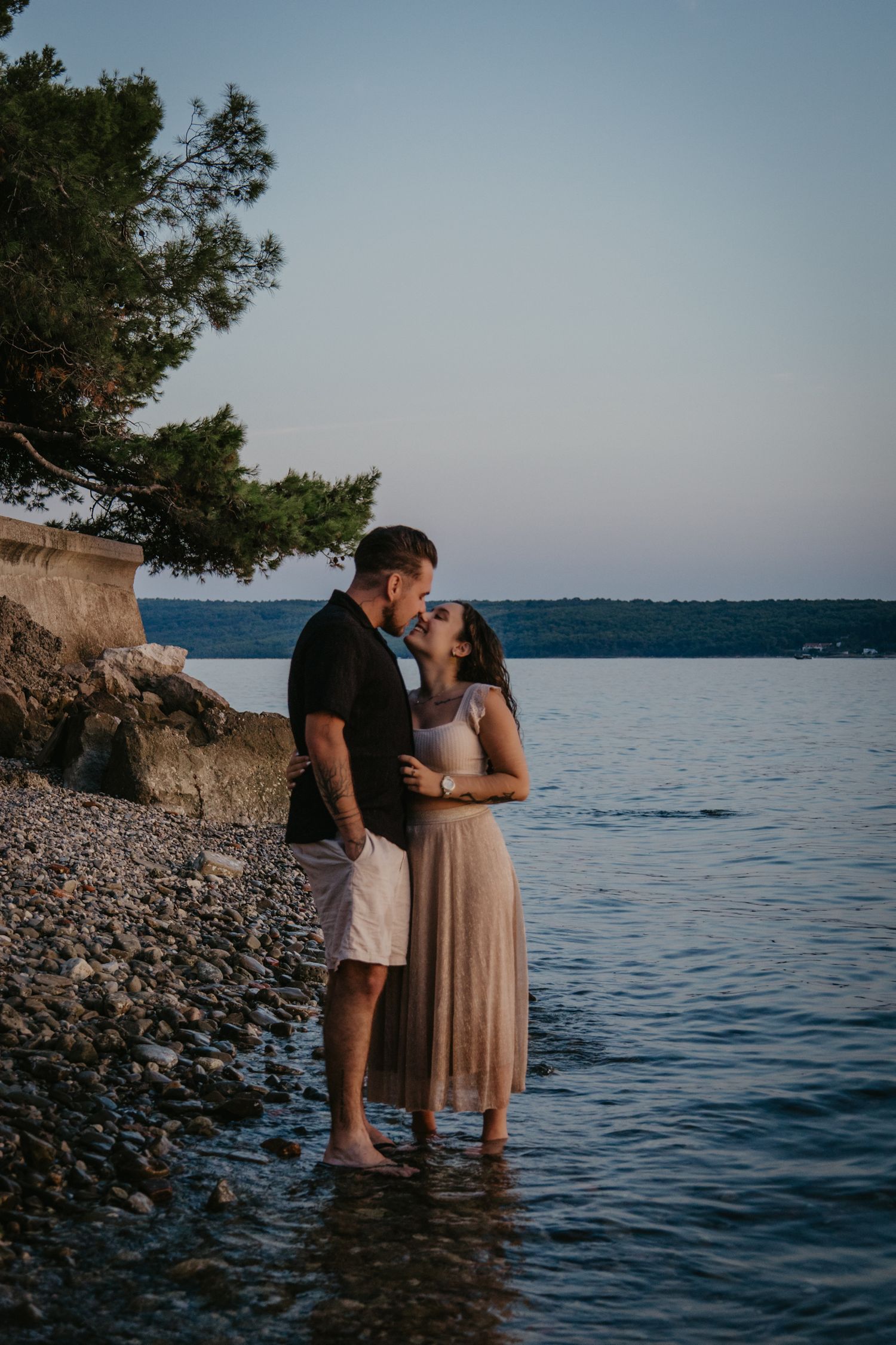 Romantic couple sharing intimate moments at rocky beach during golden hour.