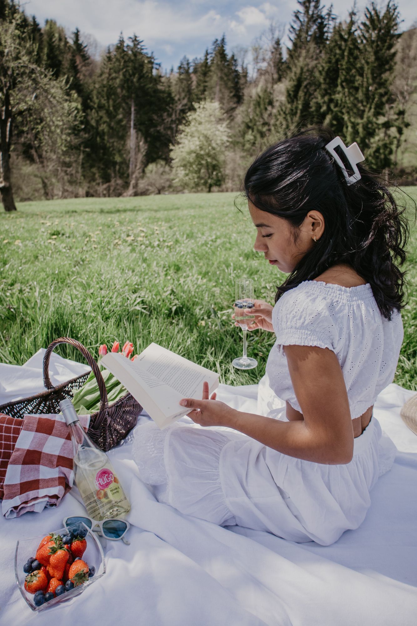 A relaxing spring picnic scene with someone reading while lying on a white blanket surrounded by snacks.