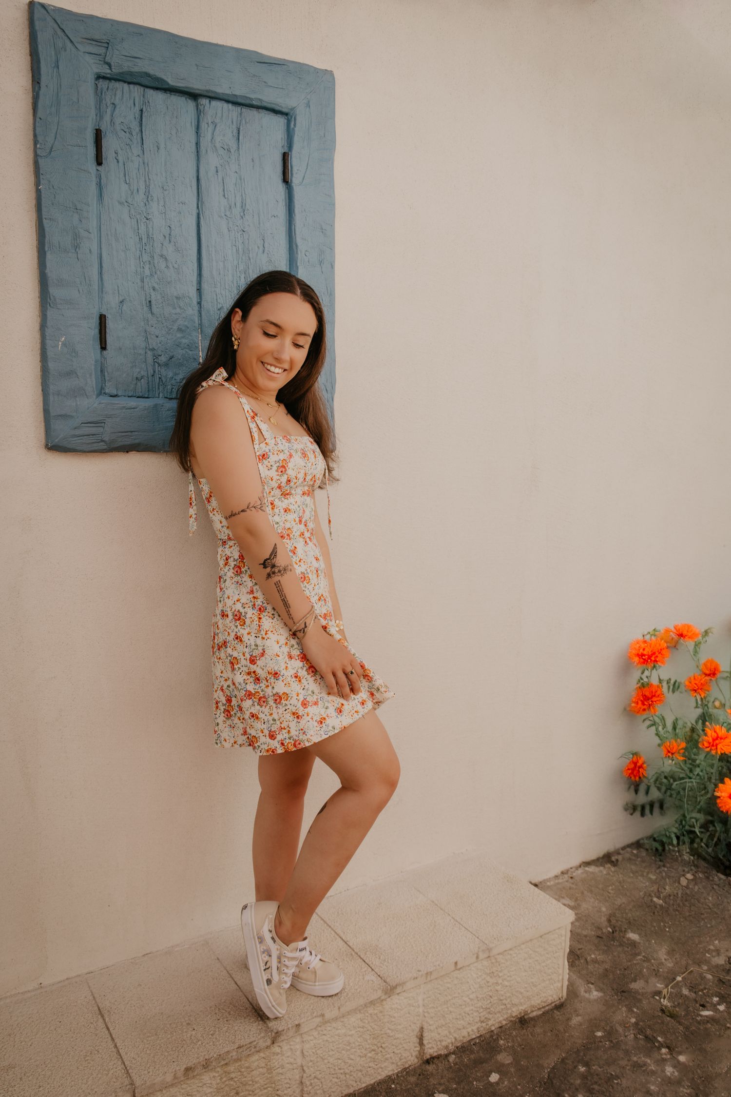 Summer fashion portrait against a white wall with blue shutters and orange flowers.