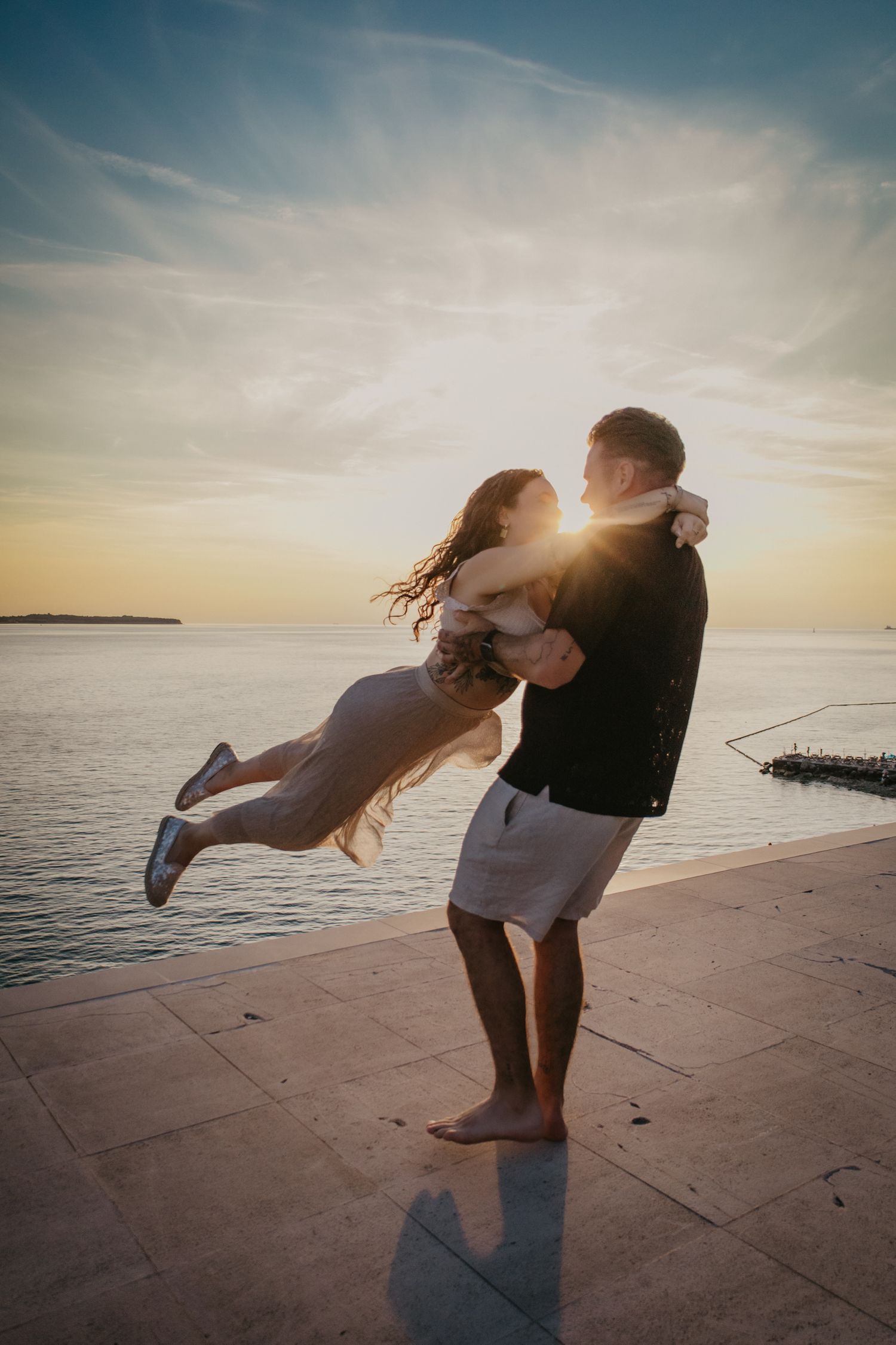 Playful sunset photoshoot with couple dancing by the waterfront.