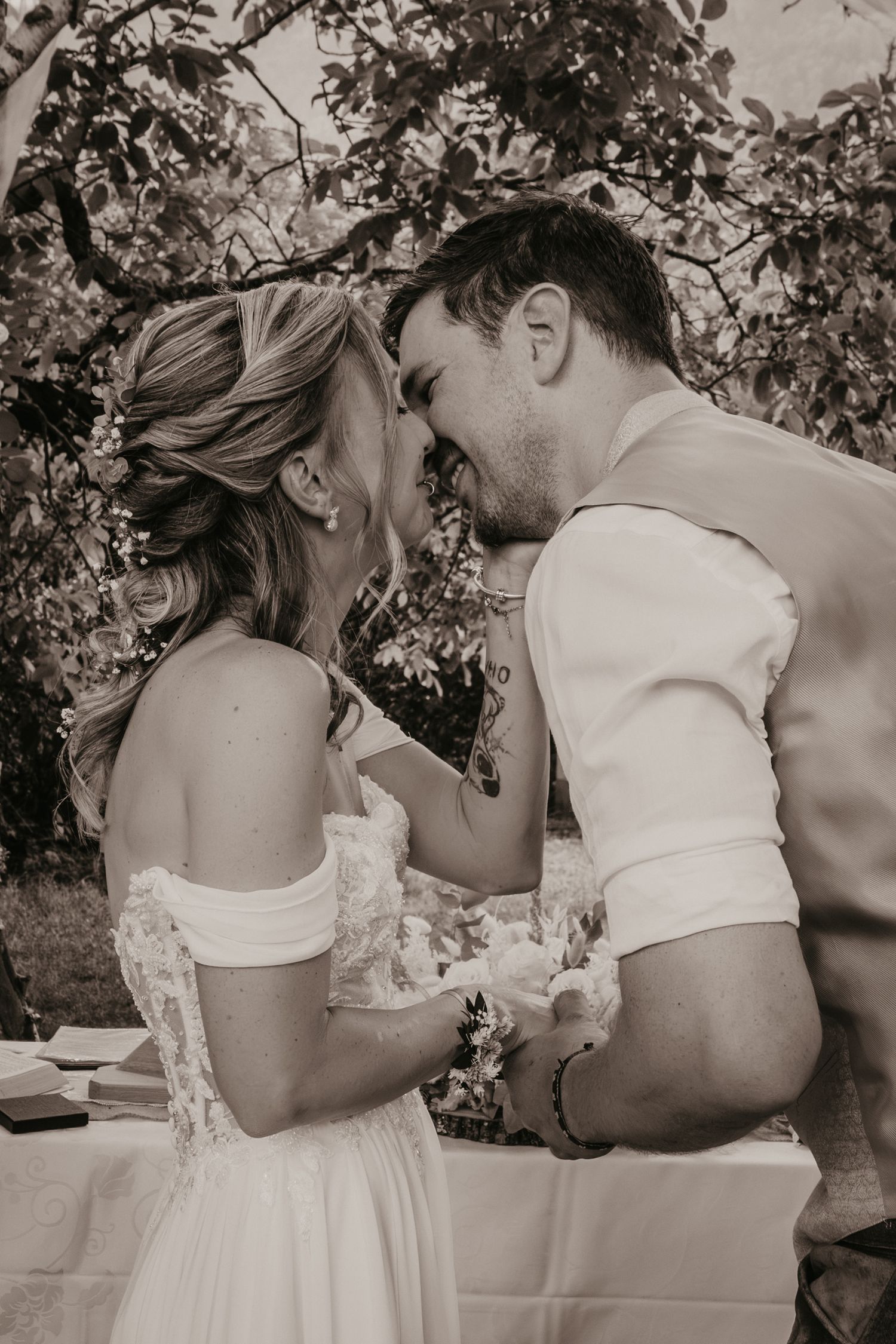 Black and white photo of a bride and groom laughing together outdoors during their wedding ceremony.