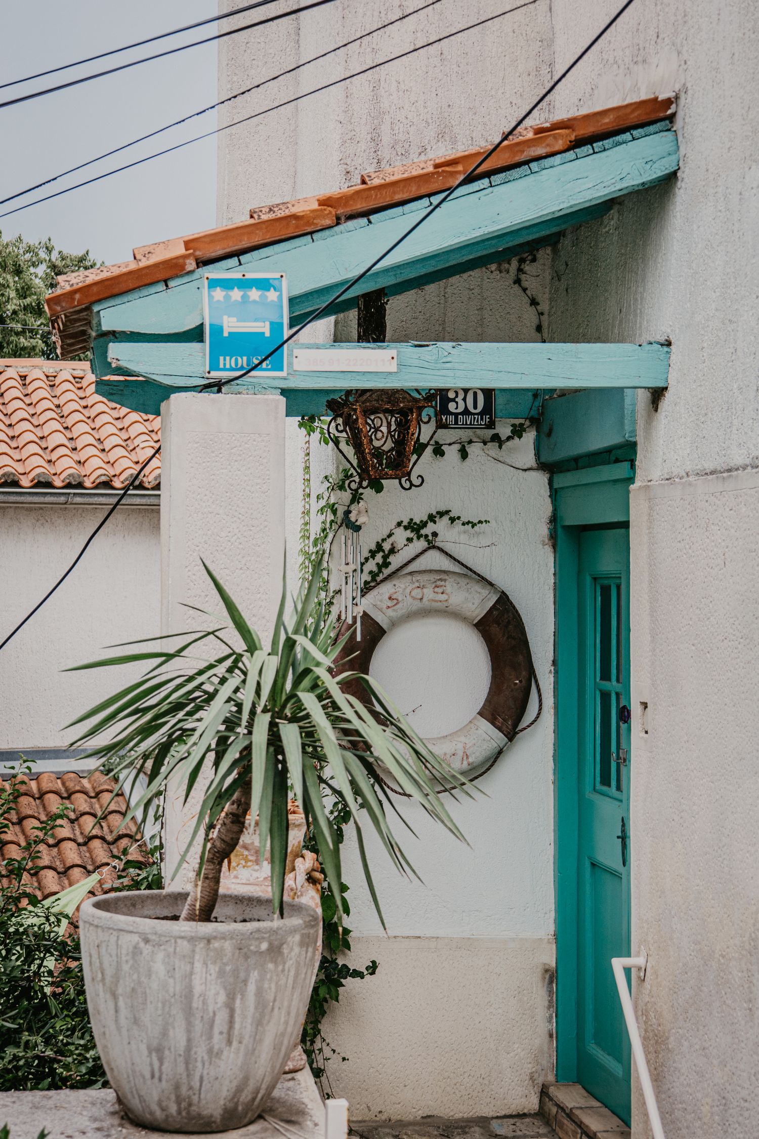 White building exterior with turquoise trim and potted plants under an awning.