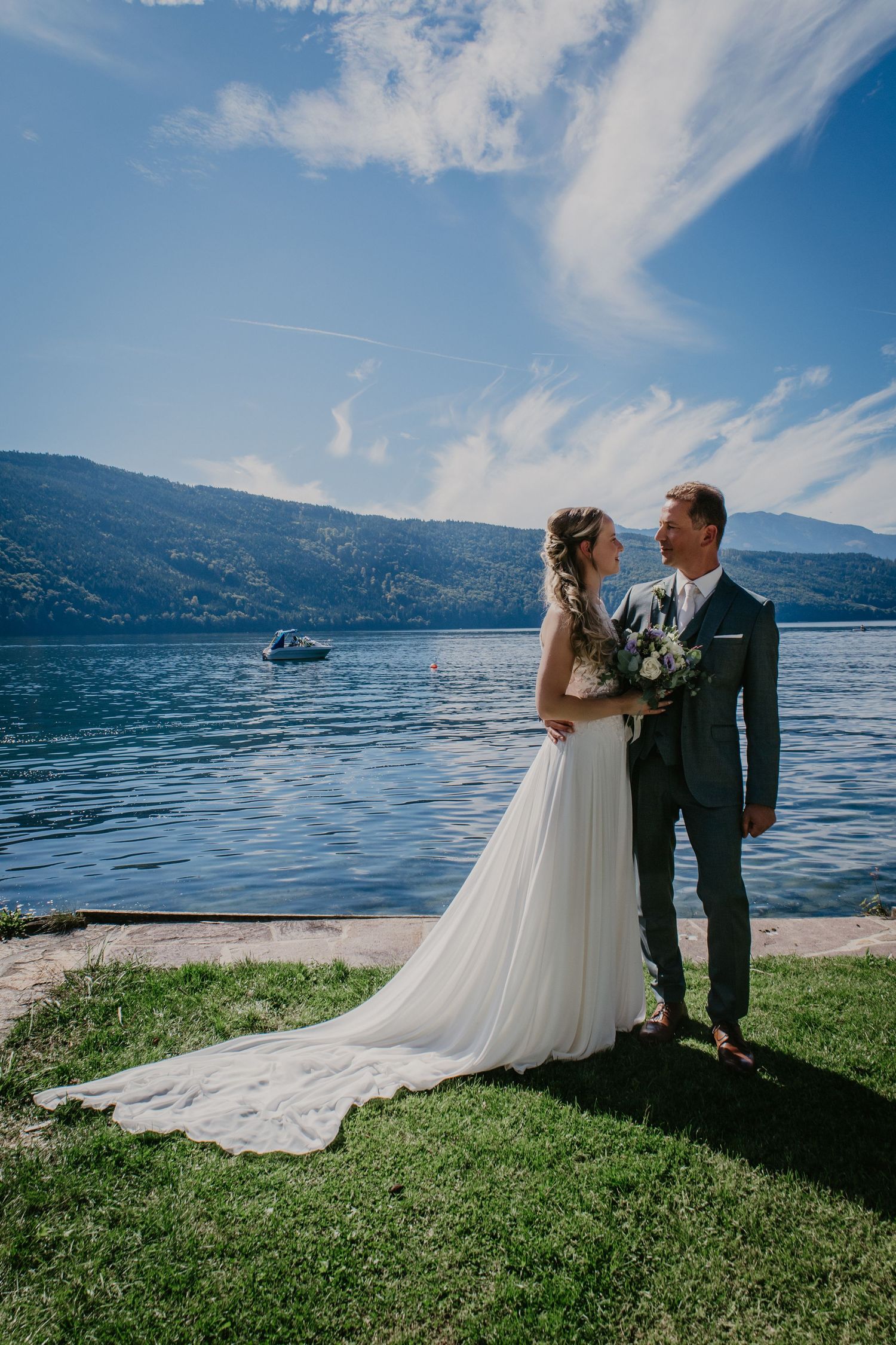 A wedding couple shares an intimate moment by a scenic lake with mountains in the background.