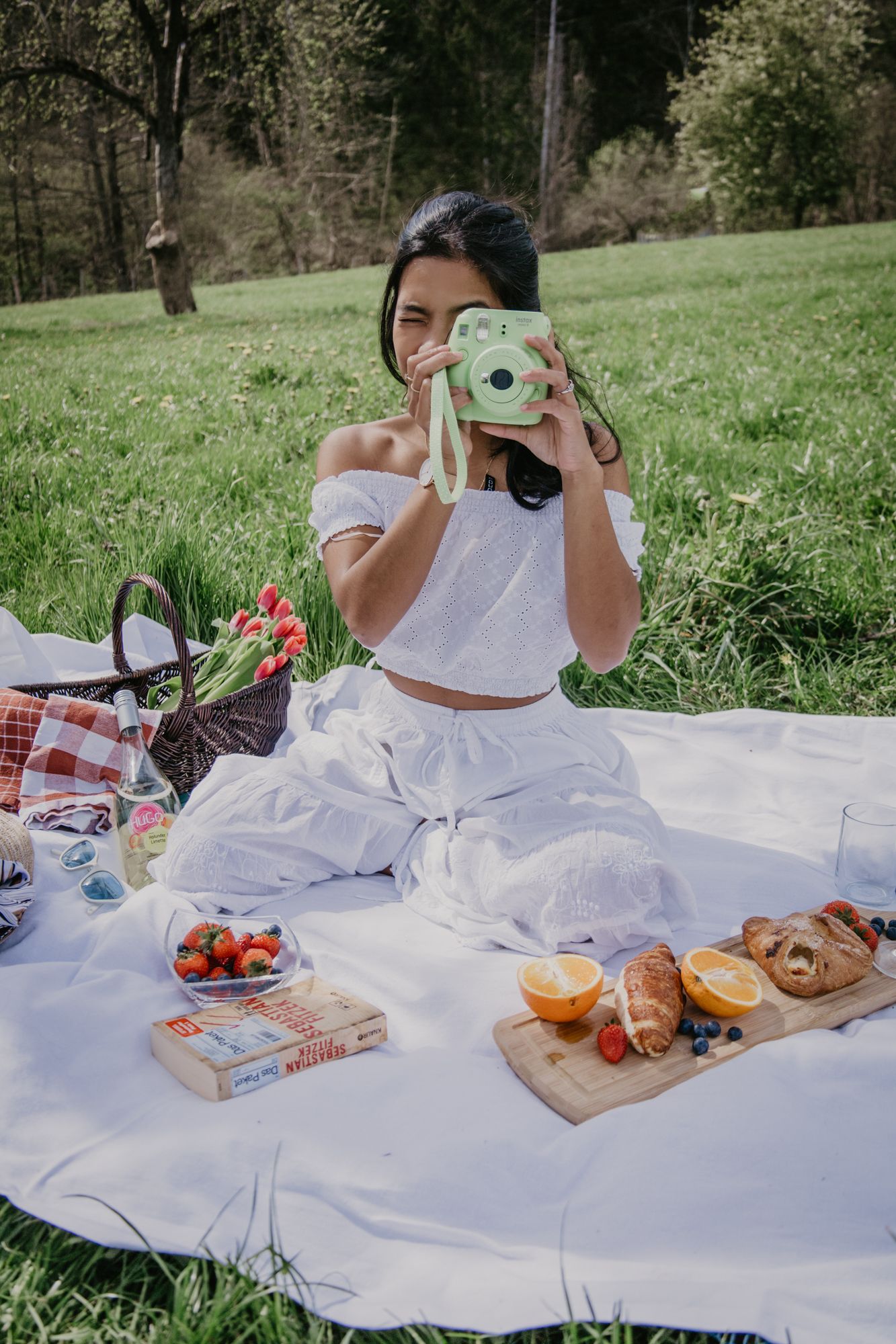 A springtime picnic scene with vintage camera, books, and fresh snacks on a white blanket.