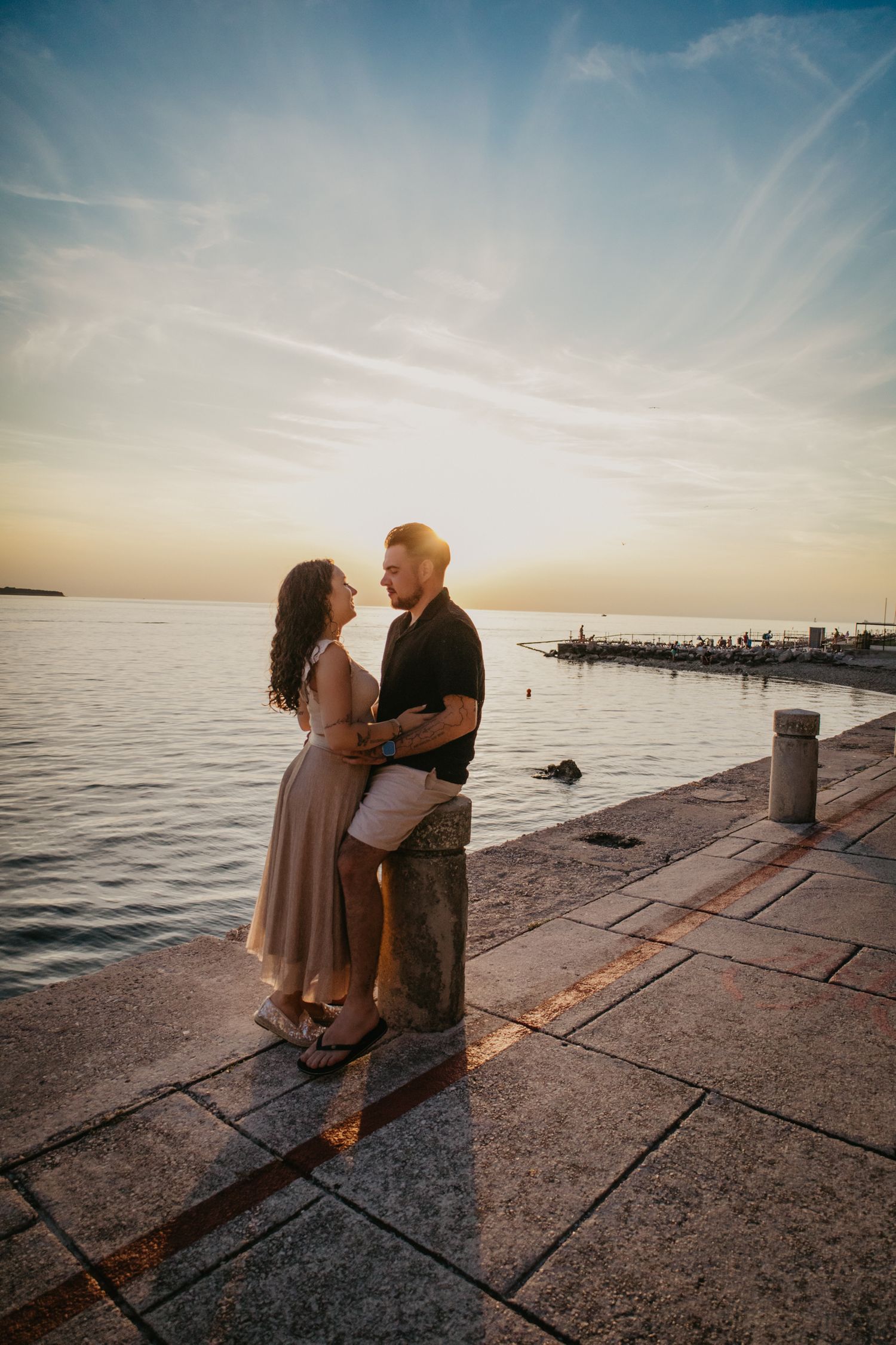 Romantic couple embracing on stone pier during sunset over calm waters.