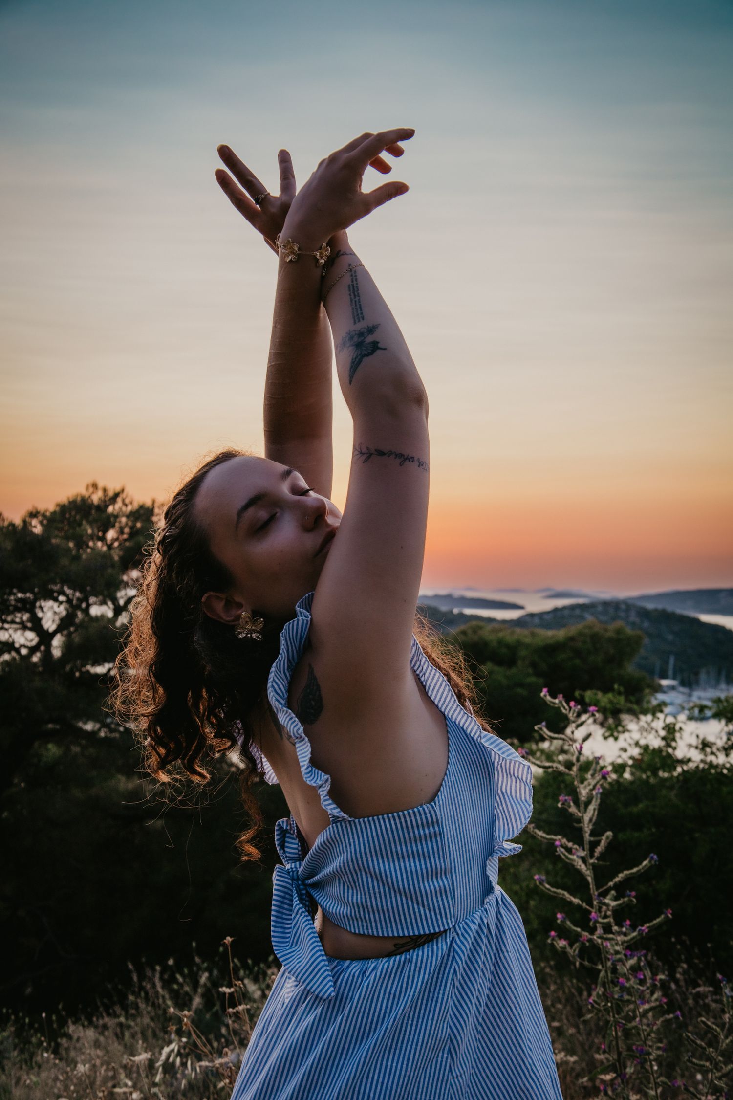 Joyful pose against sunset sky wearing a light blue ruffled summer top.