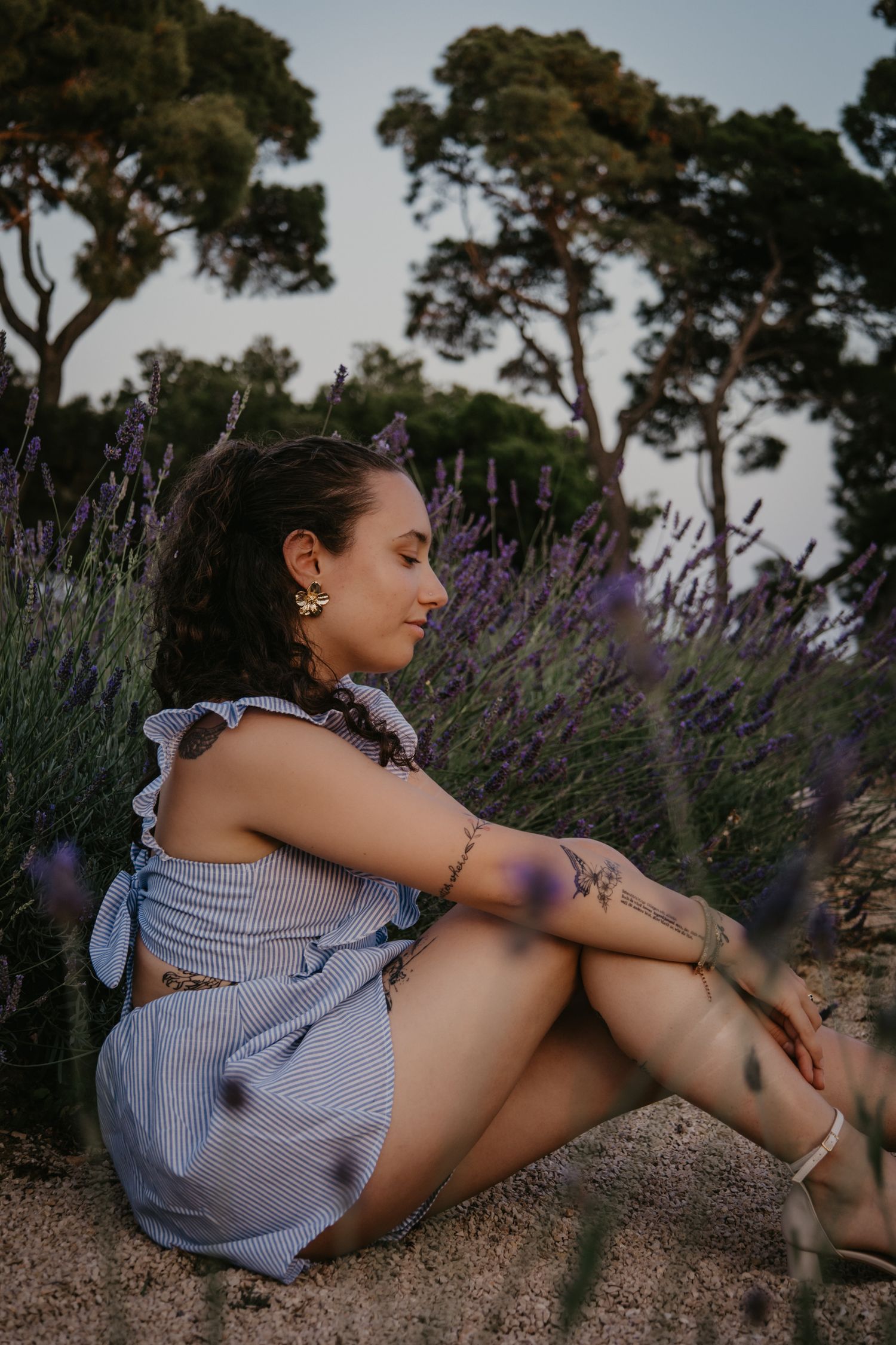 Person relaxing in a striped dress among blooming lavender bushes on a summer day.