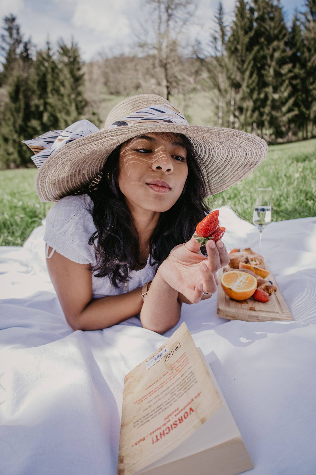 A sunny afternoon picnic featuring books, oranges, and strawberries on a crisp white blanket.