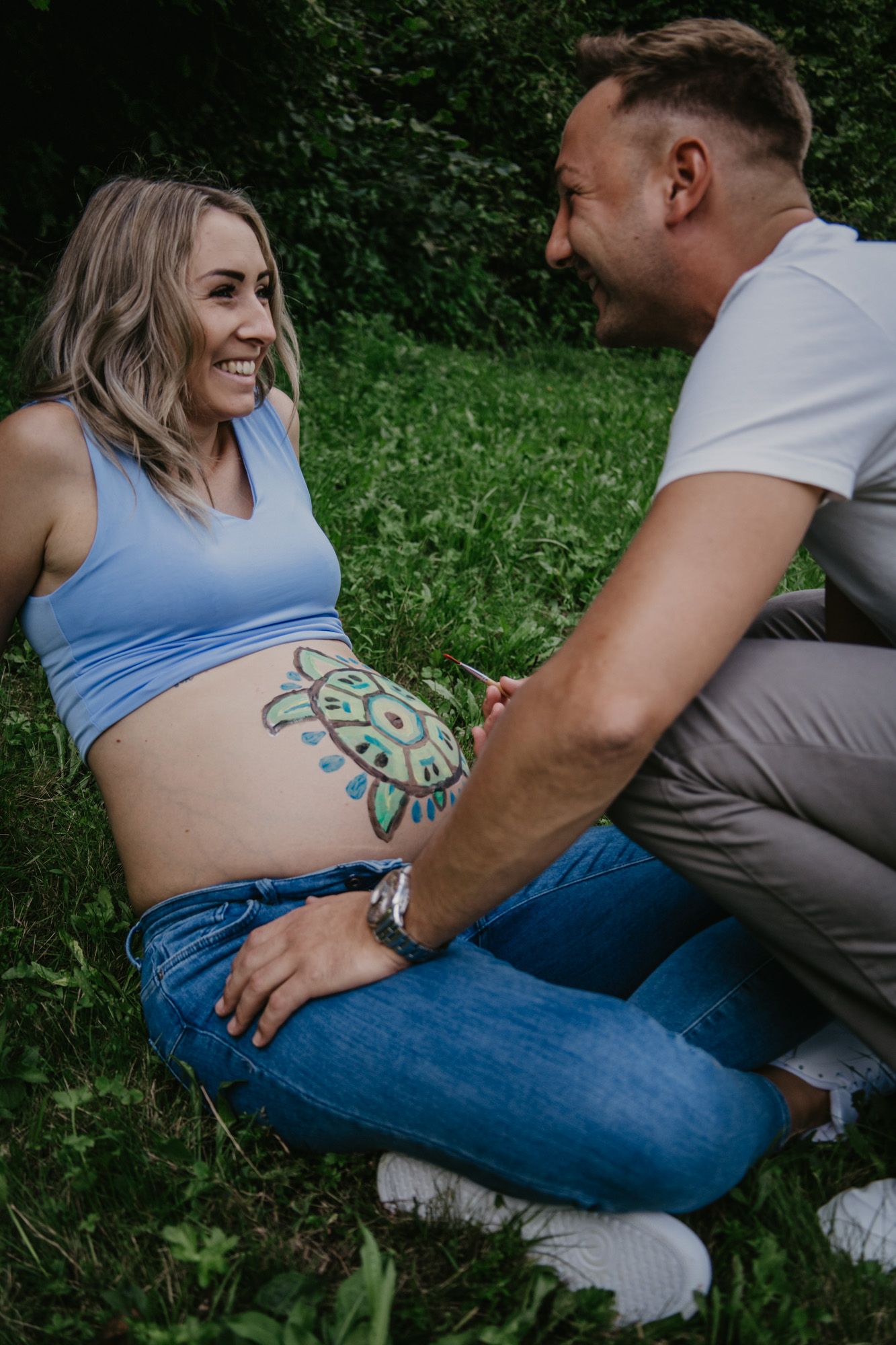 Couple sitting together on grass showing colorful tattoo art.
