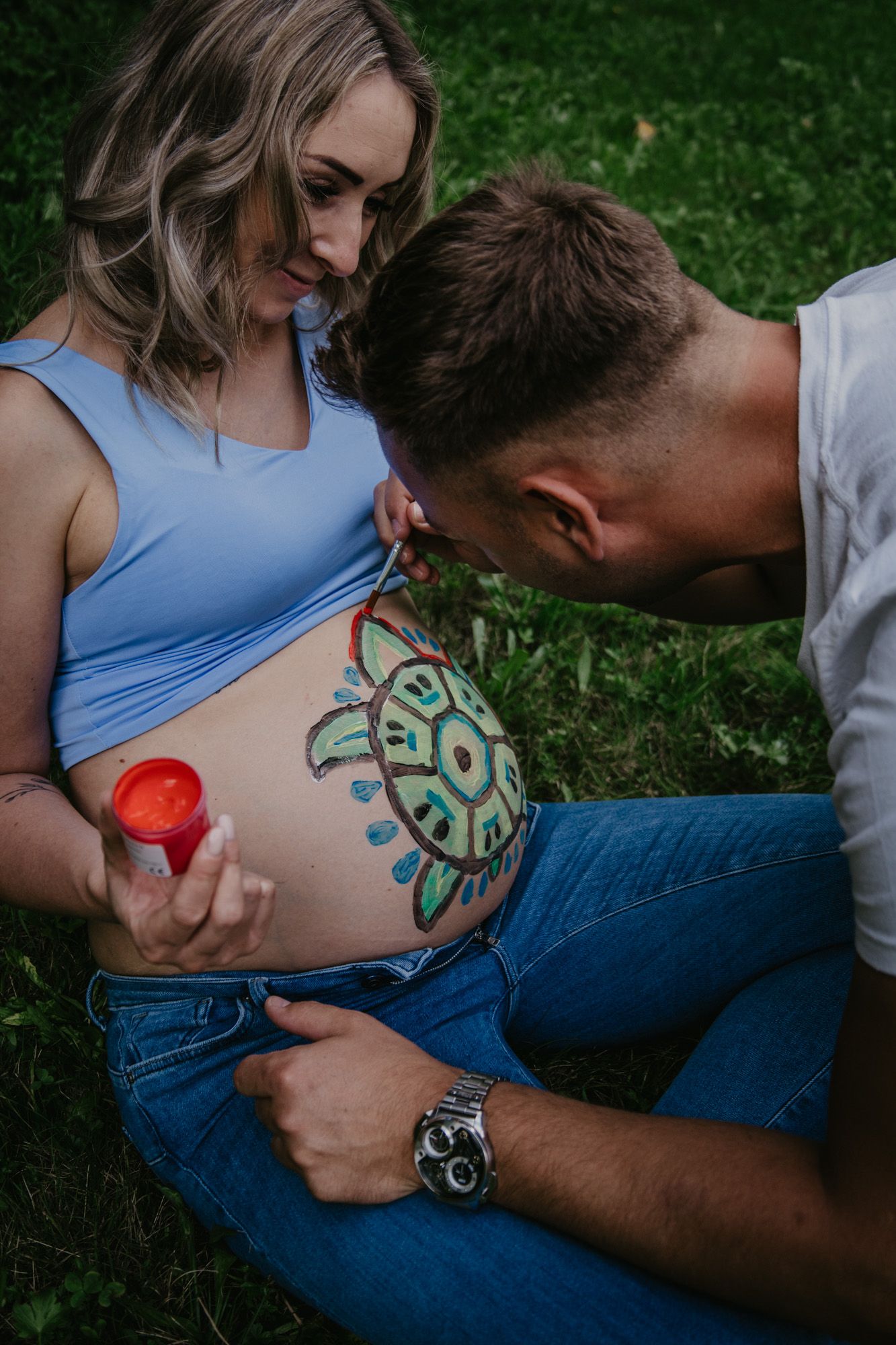 Creative pregnancy photography with belly painting in progress outdoors.