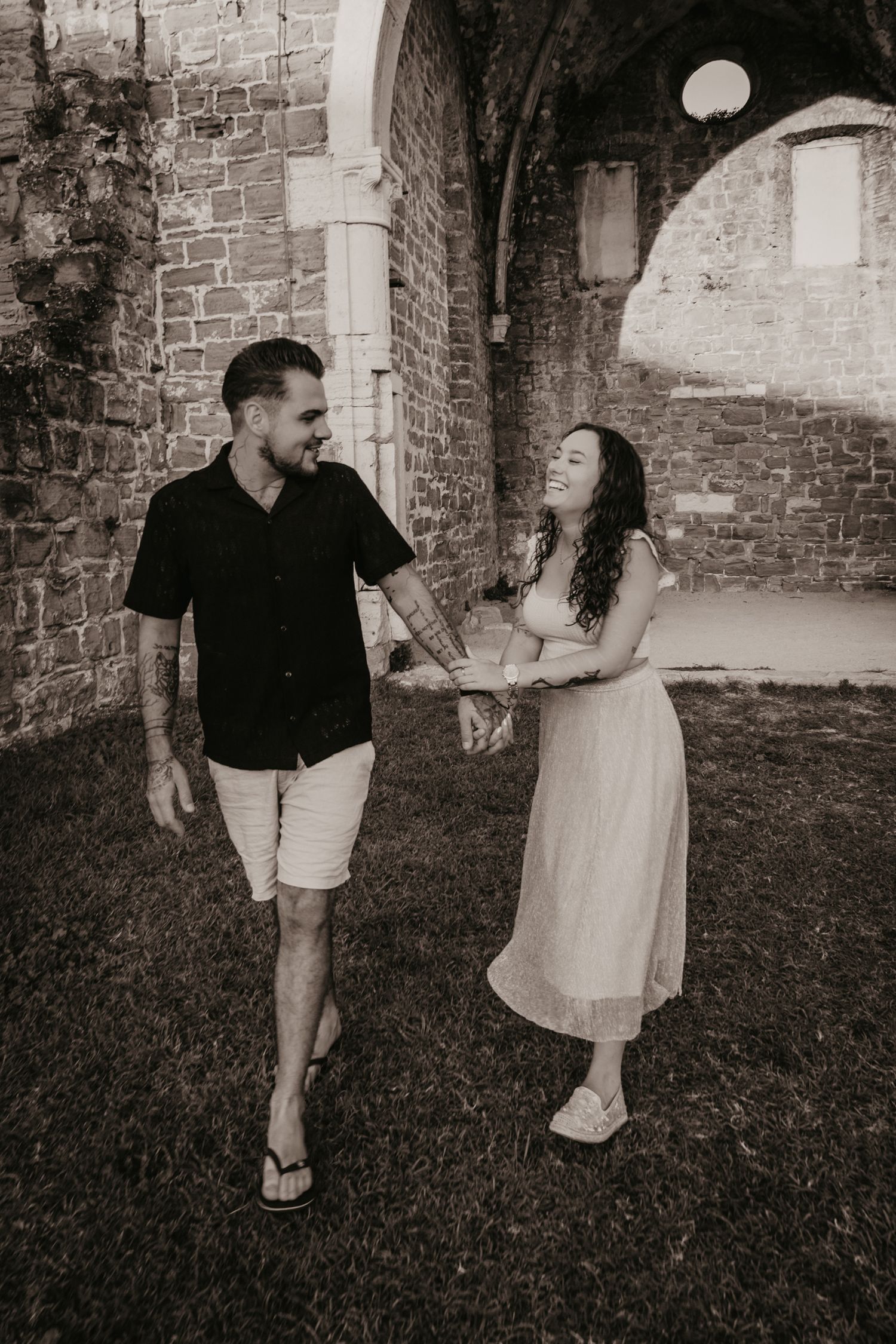 Couple sharing playful moments against rustic brick wall backdrop.
