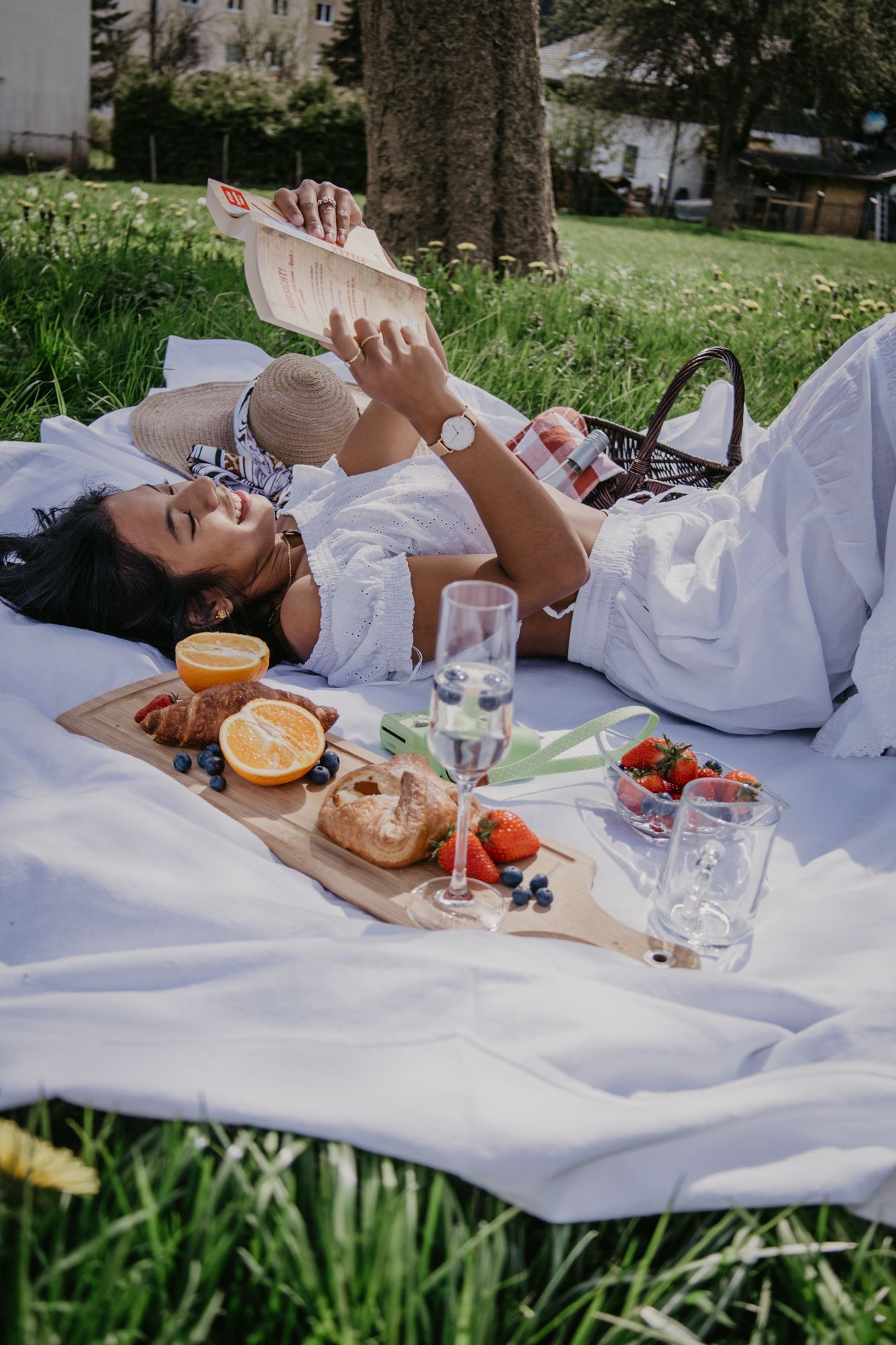 A dreamy outdoor picnic setup with fresh fruit, bread, and drinks on a white blanket in nature.