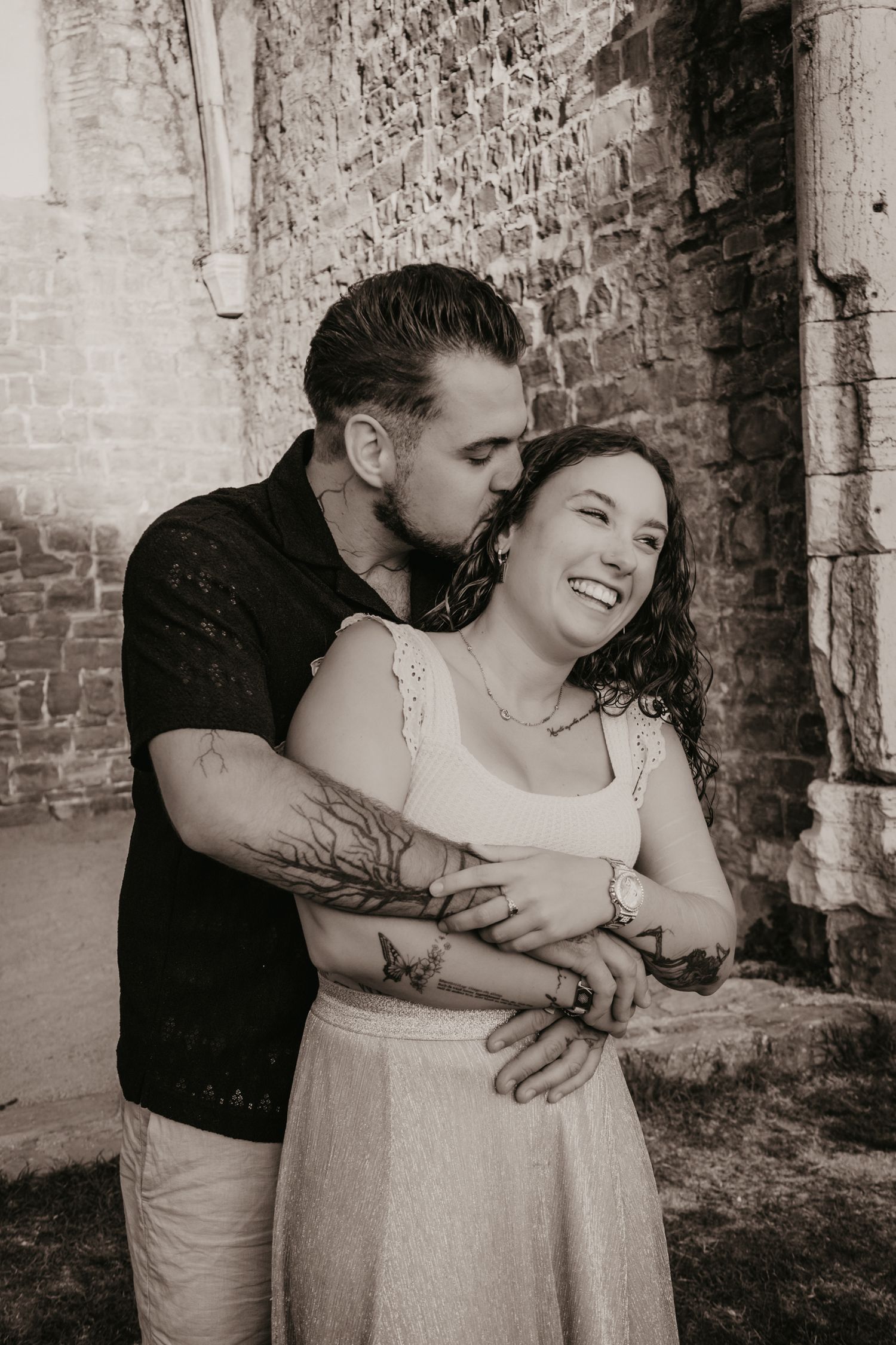 Romantic black and white portrait series showing intimate embraces against a rustic brick wall backdrop.