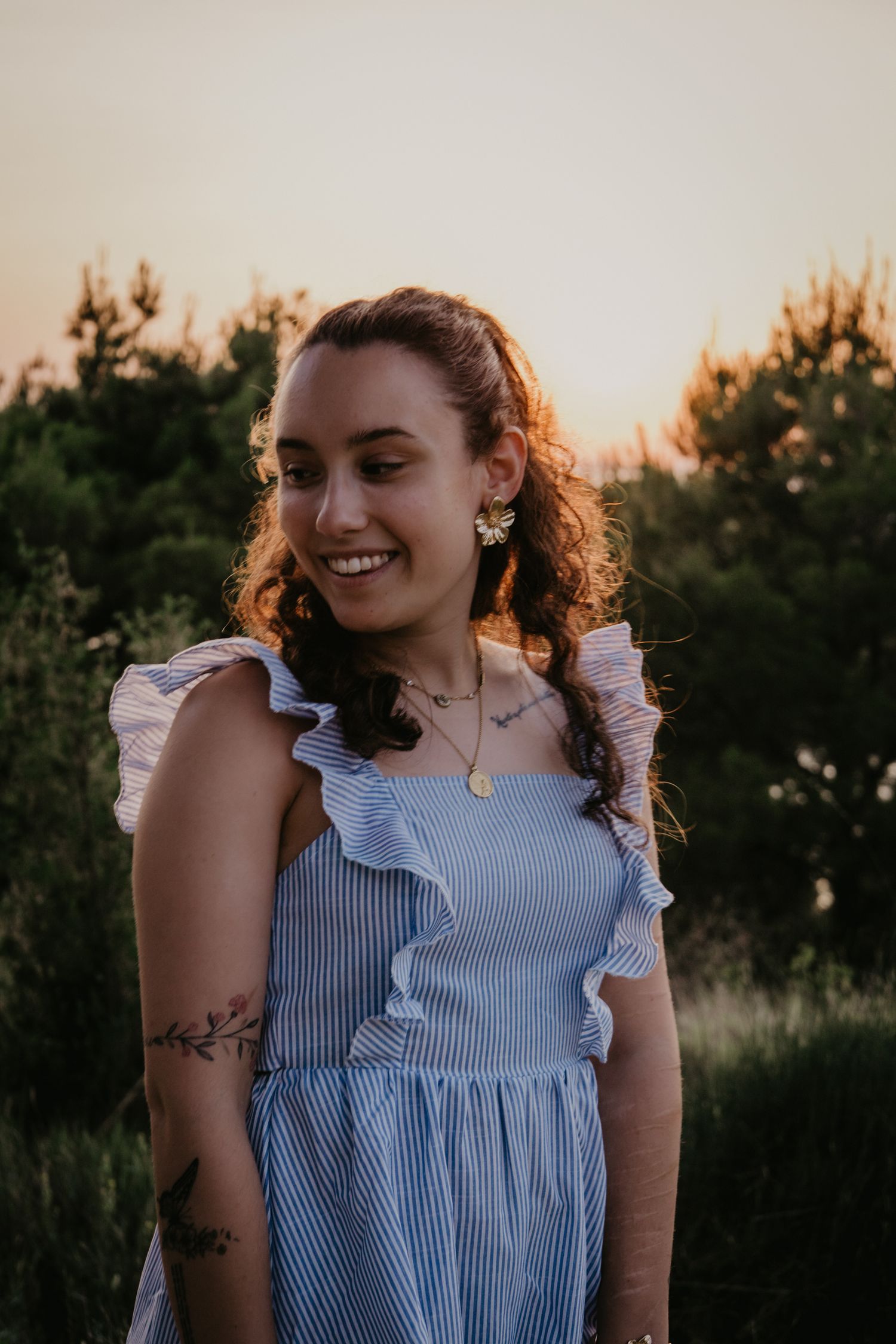 Candid portrait in a blue and white striped sleeveless top against natural foliage.