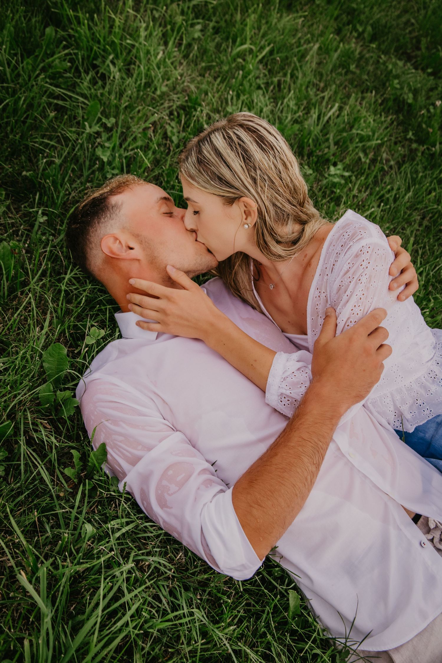 Couple sharing a romantic kiss while lying on lush green grass outdoors.