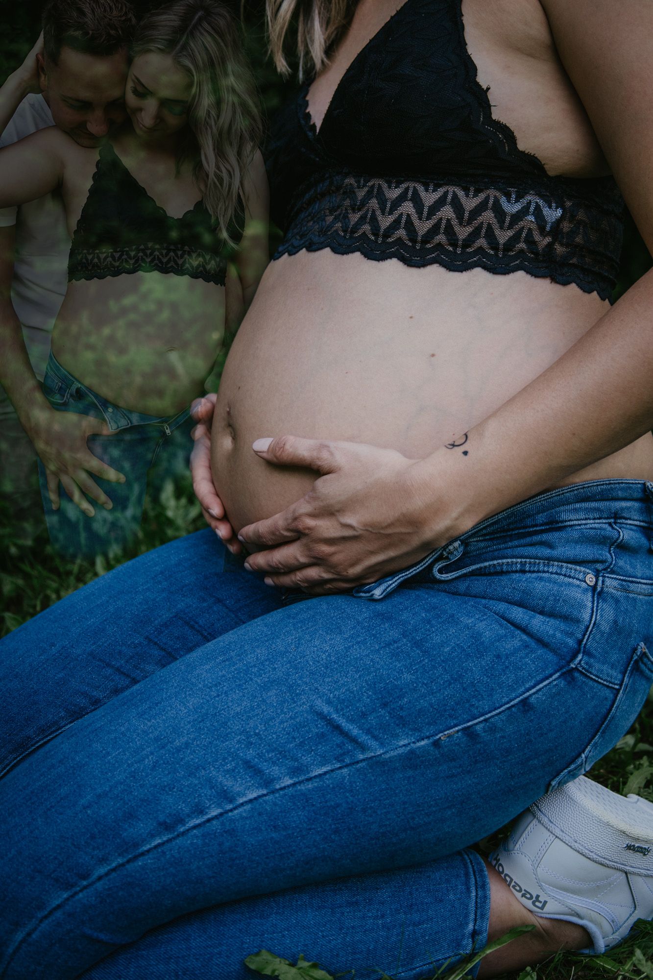 Artistic maternity photos in dark tones showing tender moments outdoors.