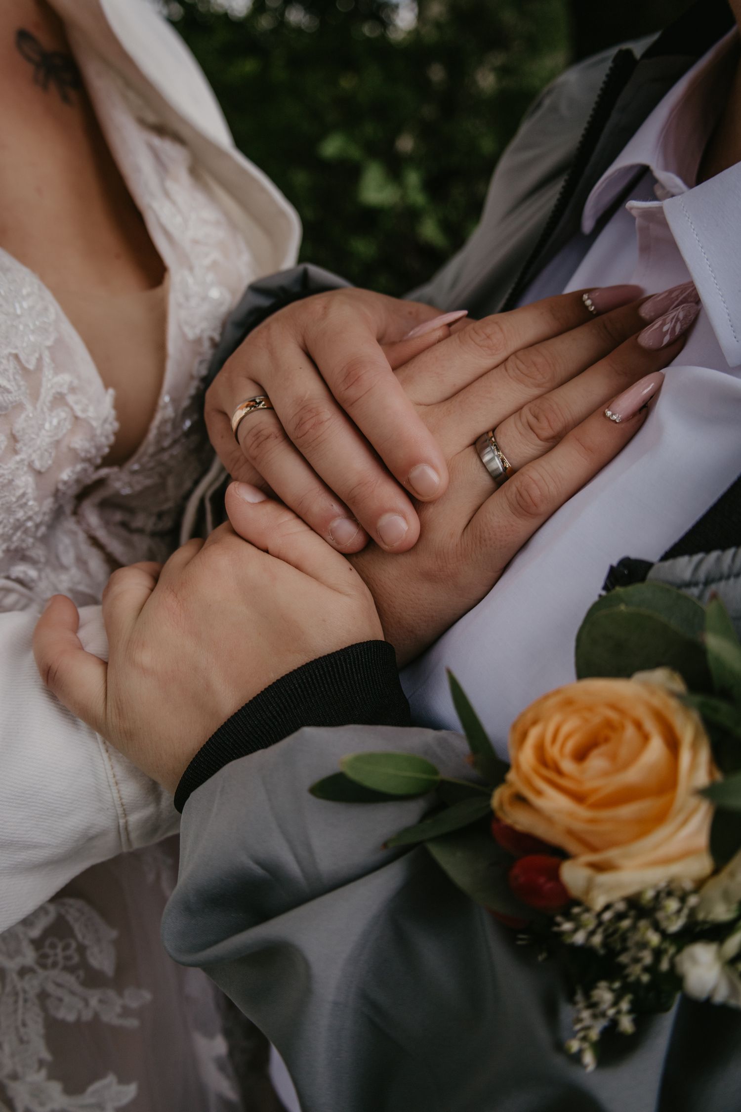 Newlywed couple's hands with rings intertwined against wedding attire.