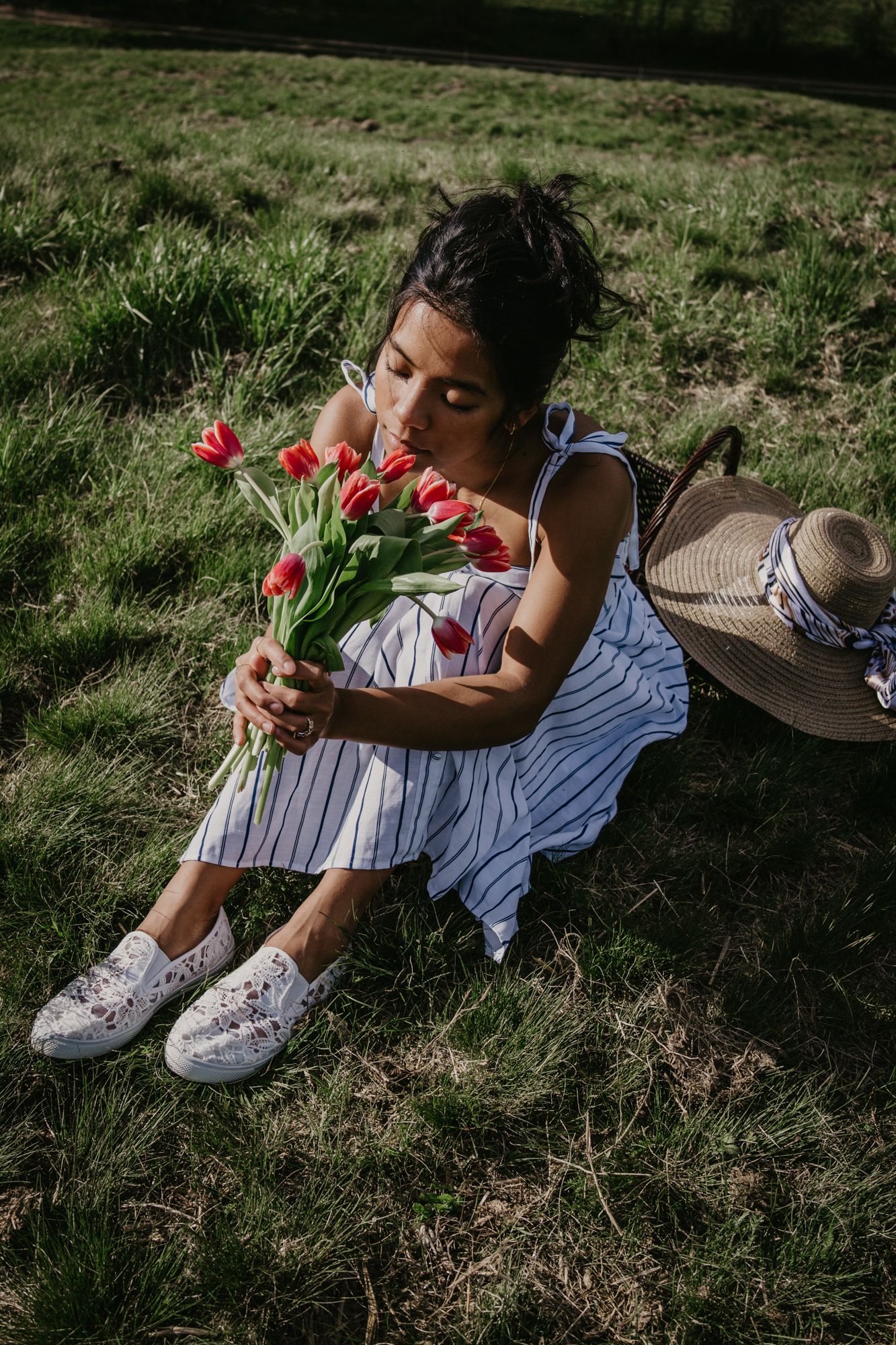 Relaxing in a grassy meadow wearing white sneakers and holding red tulips.