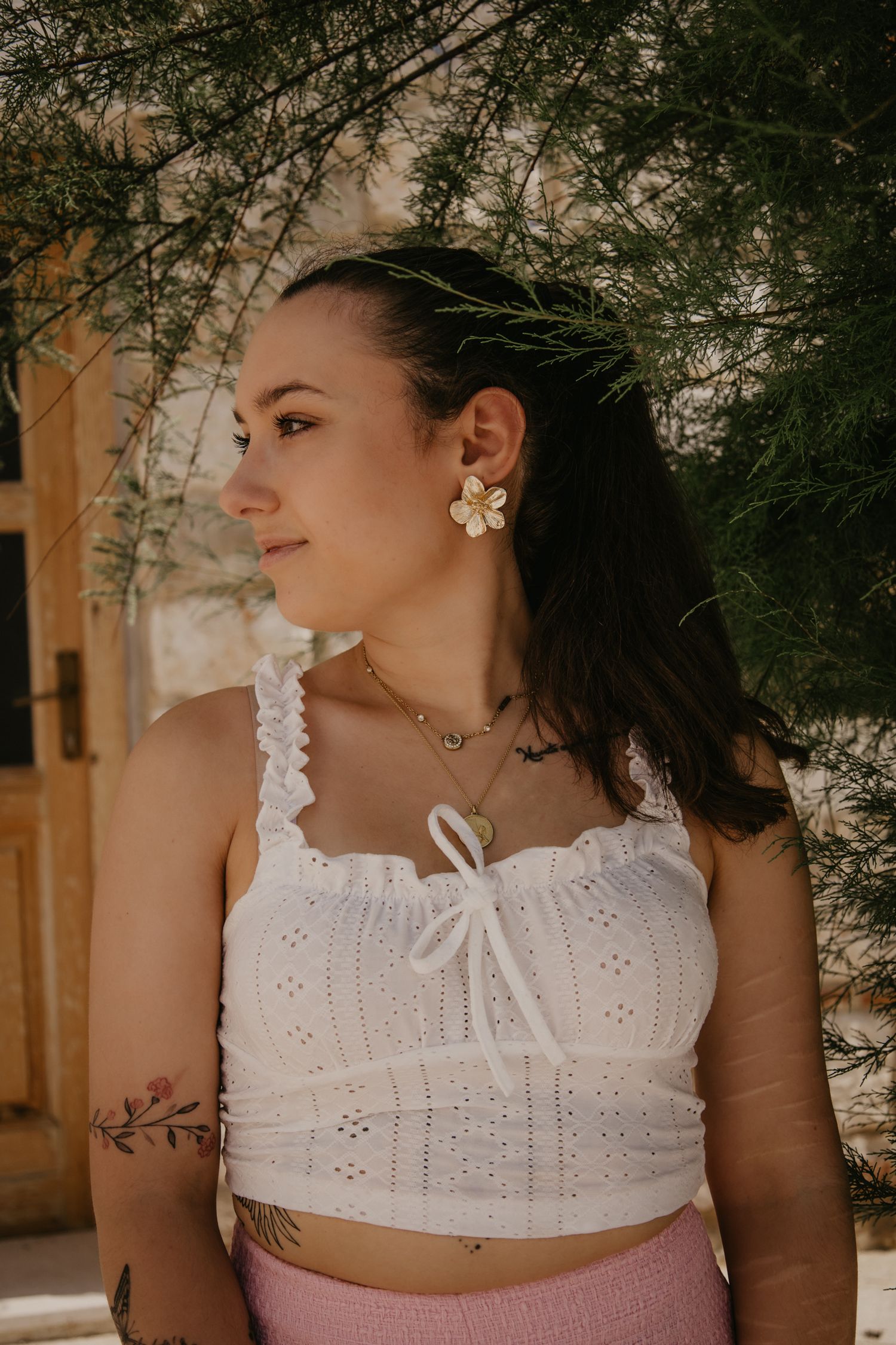 Close-up portrait with white eyelet top against natural foliage background.