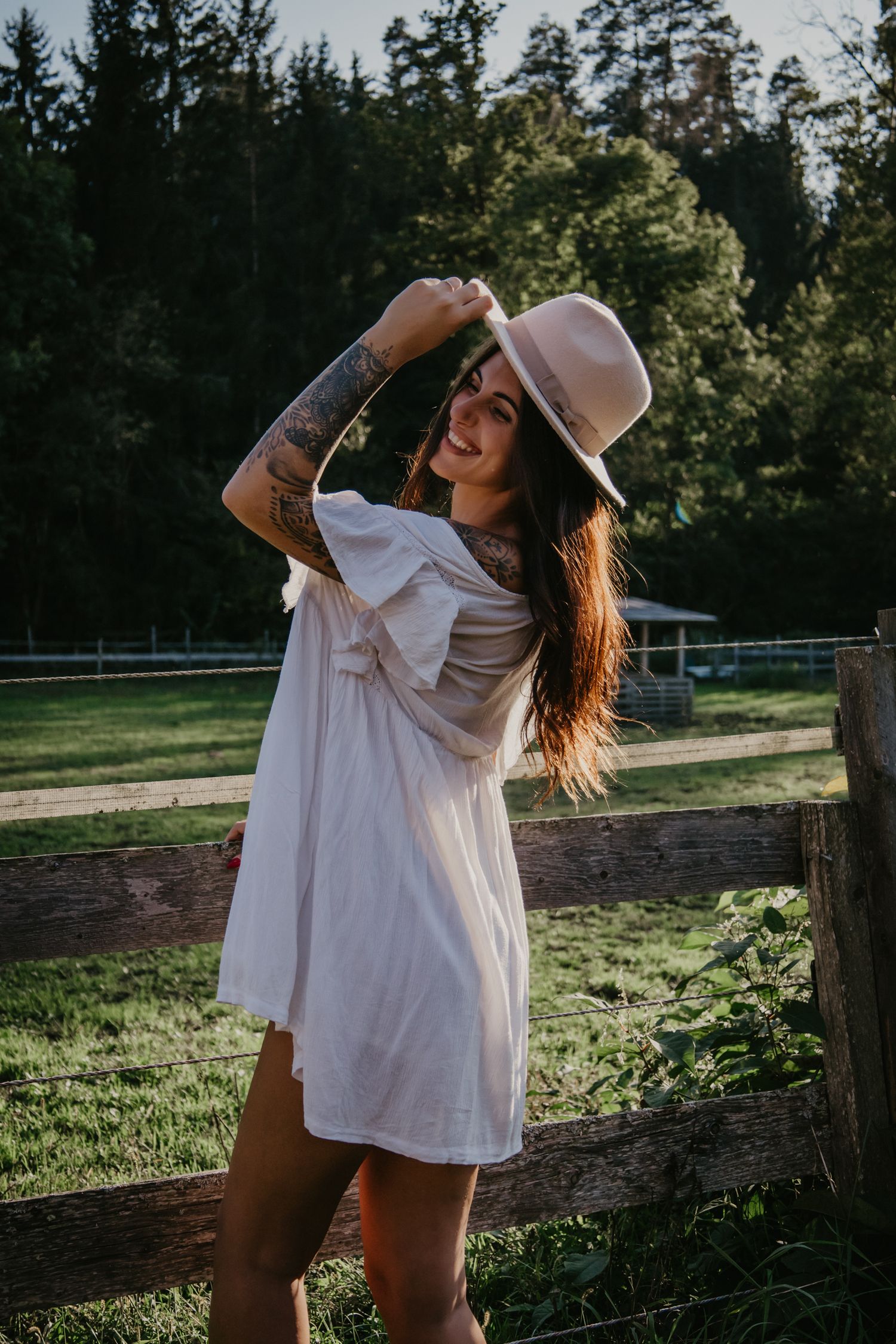 Playful outdoor photography session with flowing white dress against wooden fence and green field.