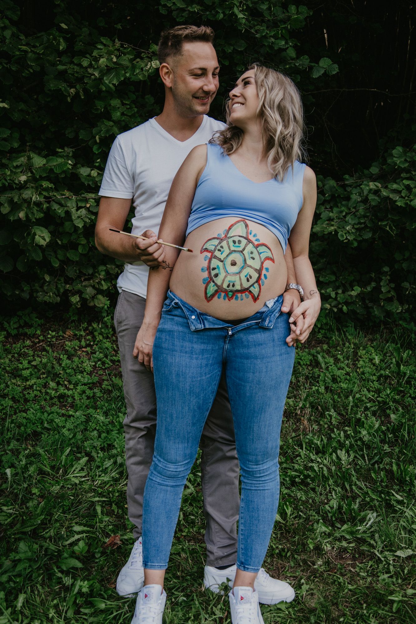 A creative pregnancy photo showing a colorful painted design on a pregnant belly in a natural outdoor setting.