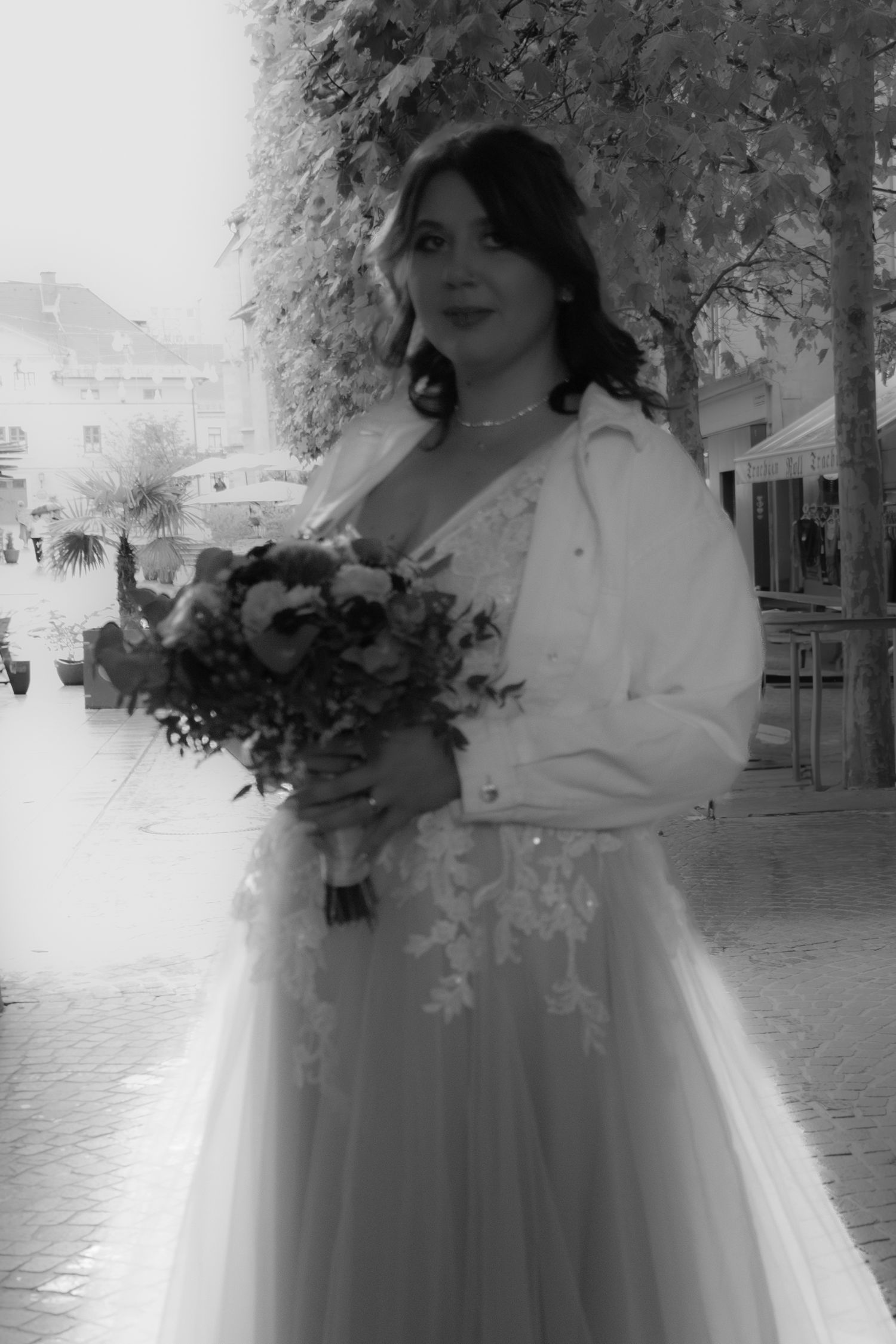Bride in white dress and jacket holding winter wedding bouquet outdoors.